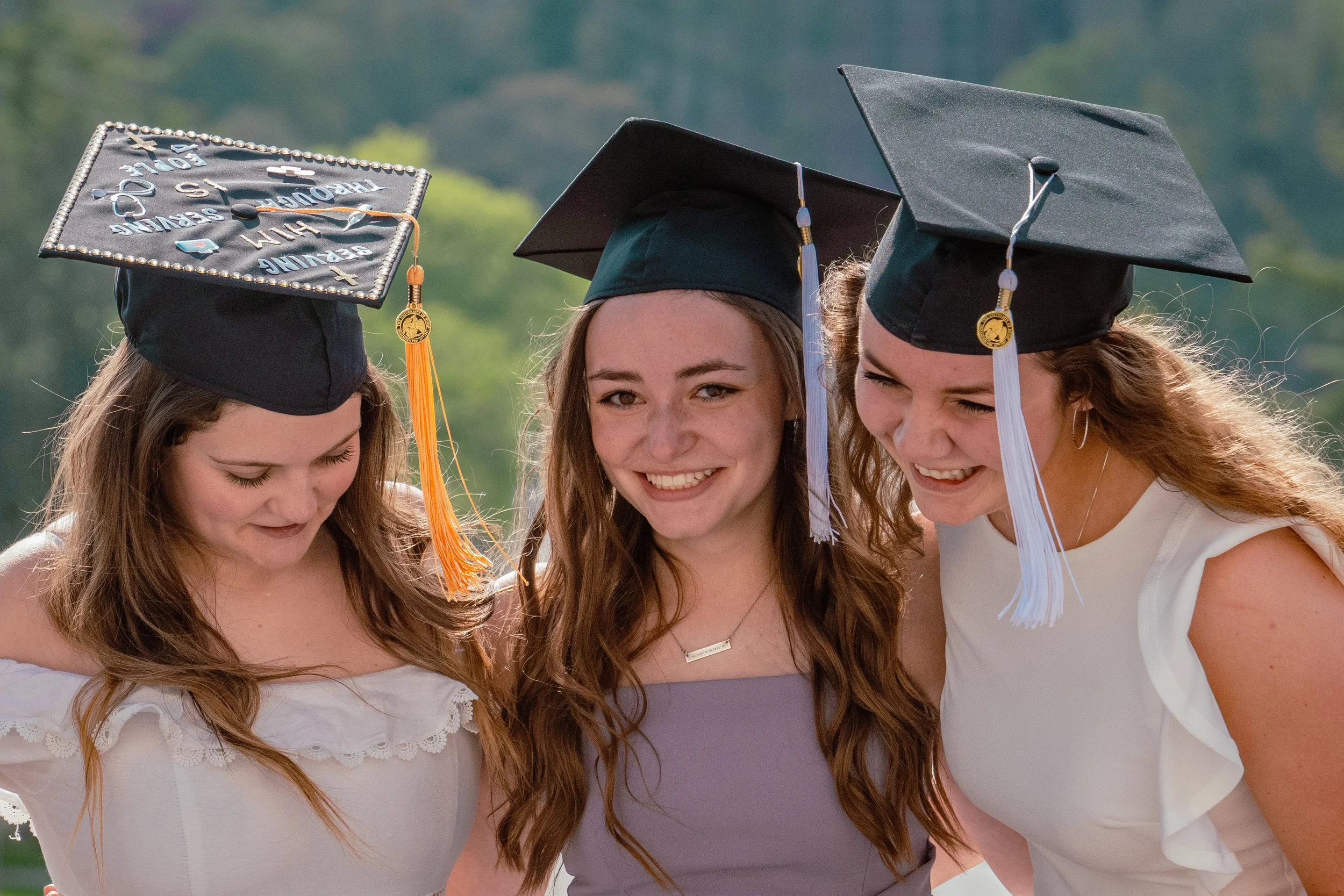 A GROUP OF 3 WOMEN TAKE GRADUATION PHOTO ON THE UNIVERSITY OF IOWA CAMPUS TO CELEBRATE THE MOMENT