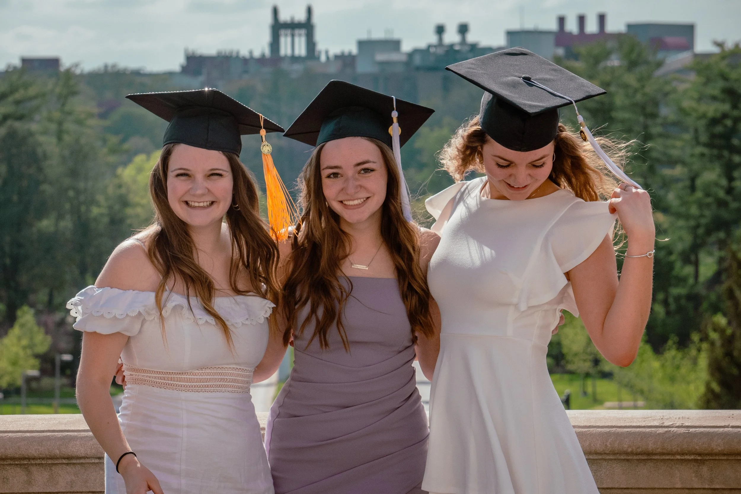 A GROUP OF 3 WOMEN TAKE GRADUATION PHOTO ON THE UNIVERSITY OF IOWA CAMPUS TO CELEBRATE THE MOMENT