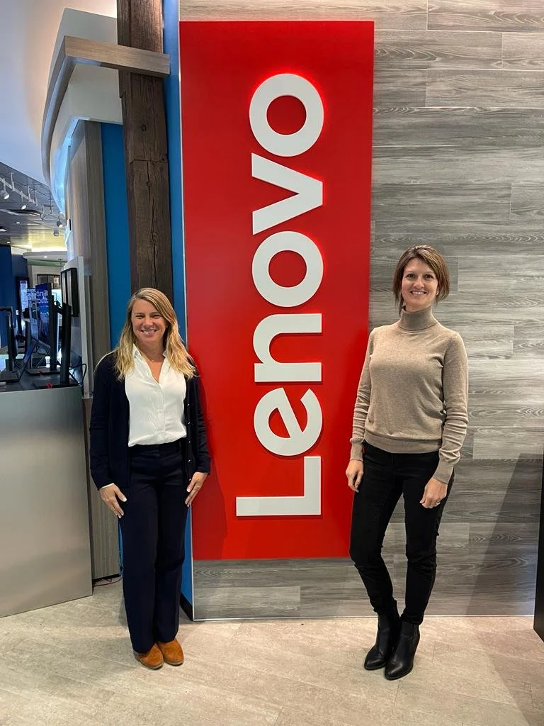 Two women standing in front of a large red vertical sign that says "Lehigh" in white letters inside a modern indoor space.