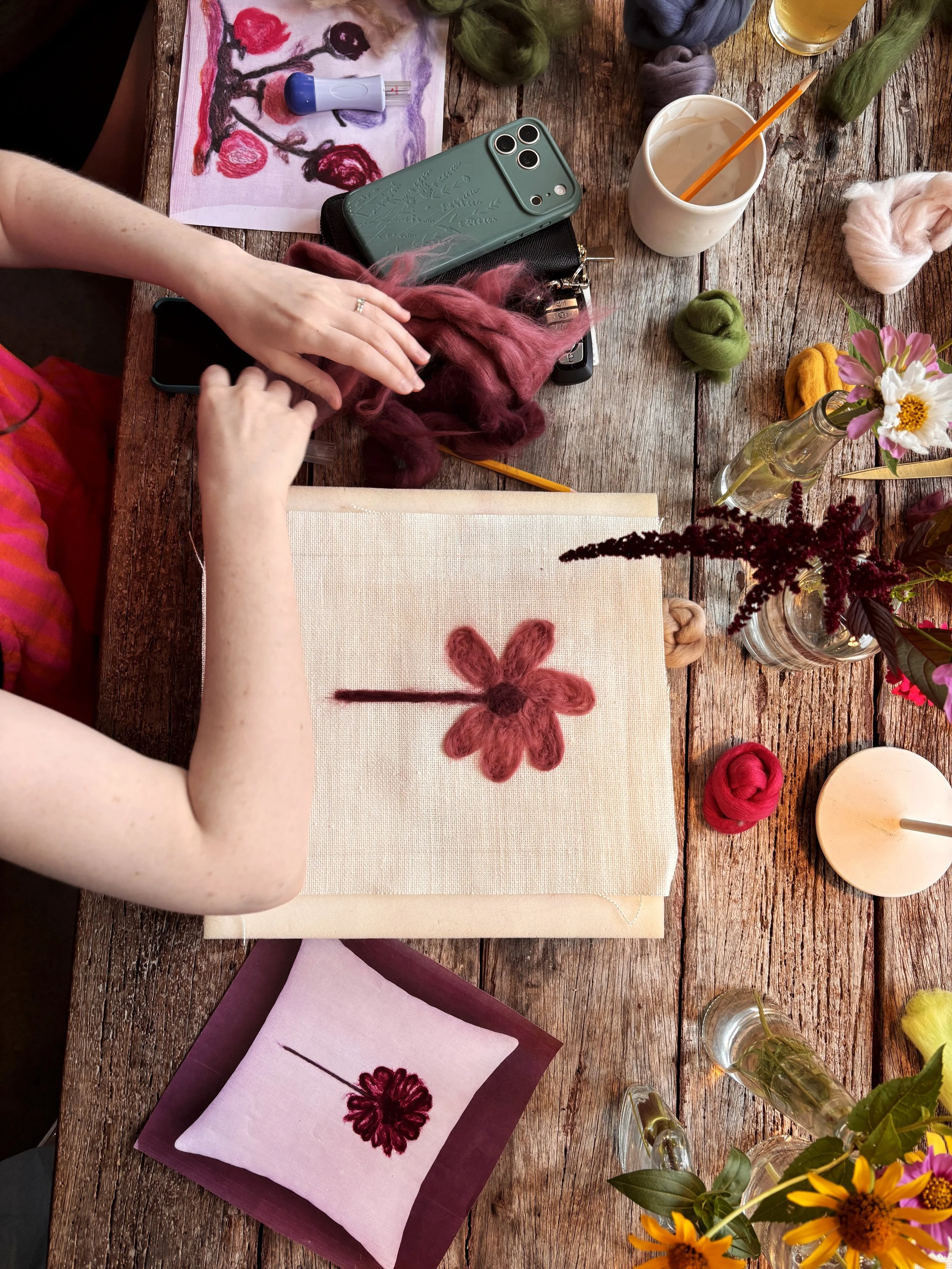 Guest creating art at a Paint with Wool workshop, Le Studio Anthost, New York, with pink and red wool yarn, brushes, and fresh flowers on the table.