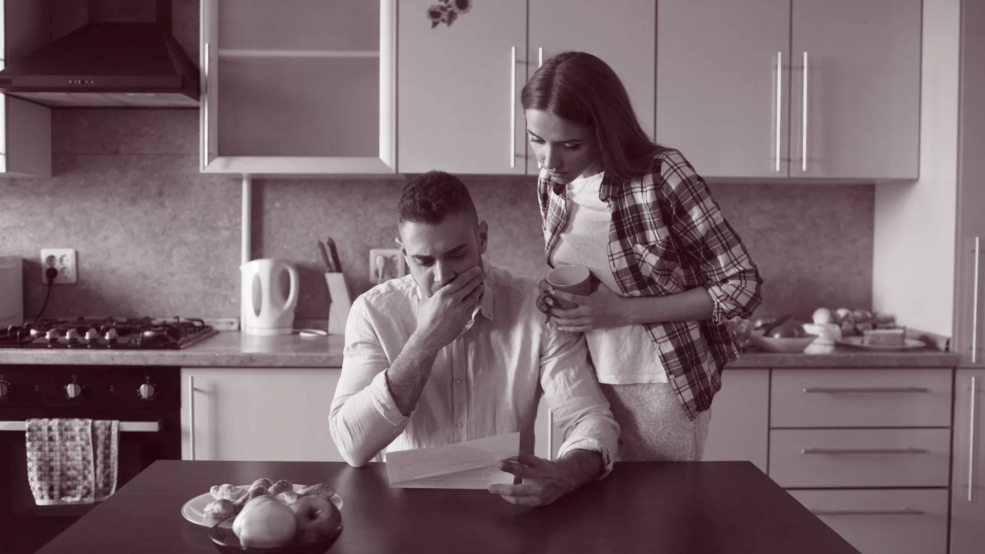 Couple sitting at a kitchen table reviewing finances together, showing tension and focus during a money conversation at home