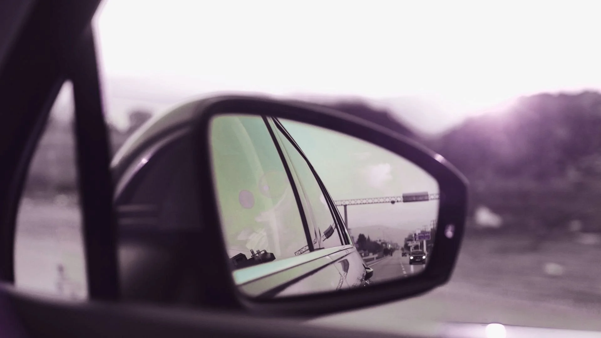Rear-view mirror reflecting the road behind a moving car at sunset, symbolizing financial blind spots and gaining perspective around money and relationships.