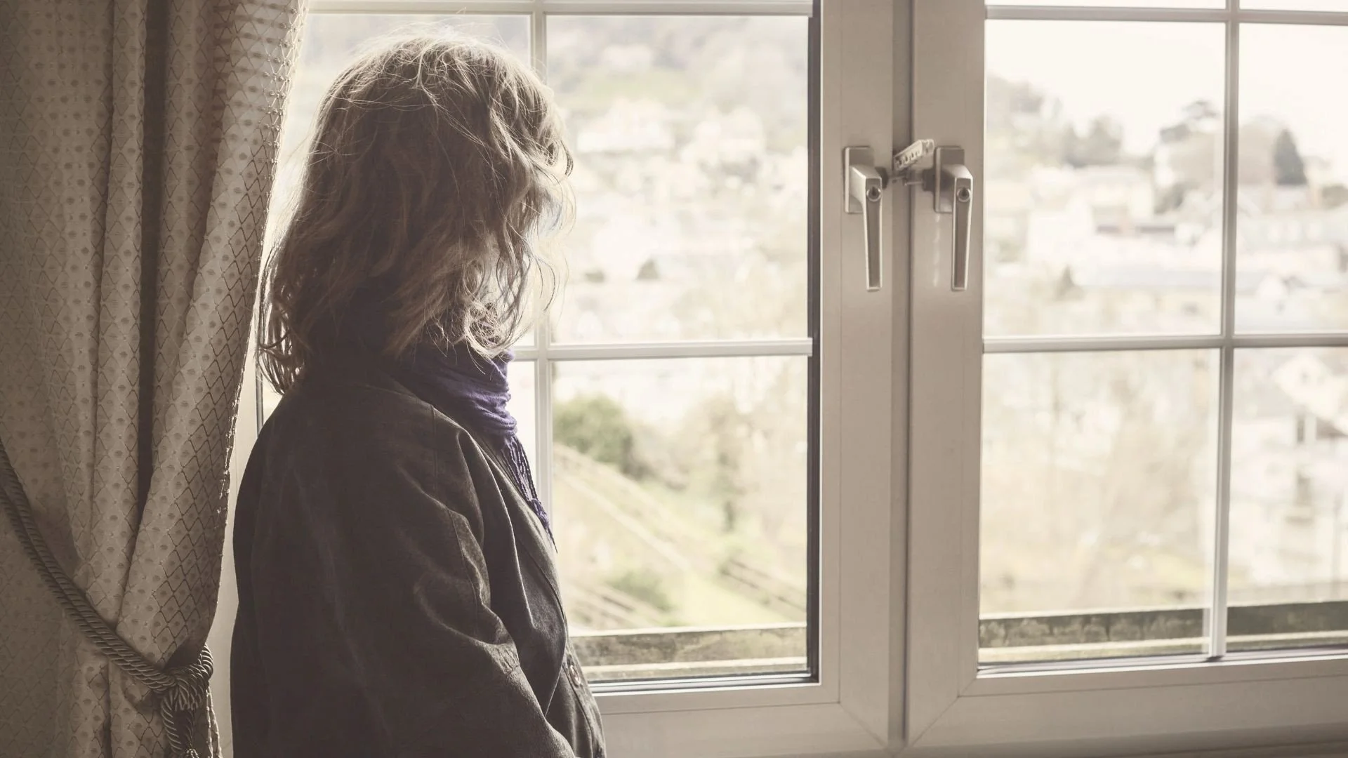 Person standing by a window, looking outside thoughtfully, representing reflection and navigating real-life decisions during uncertain moments.