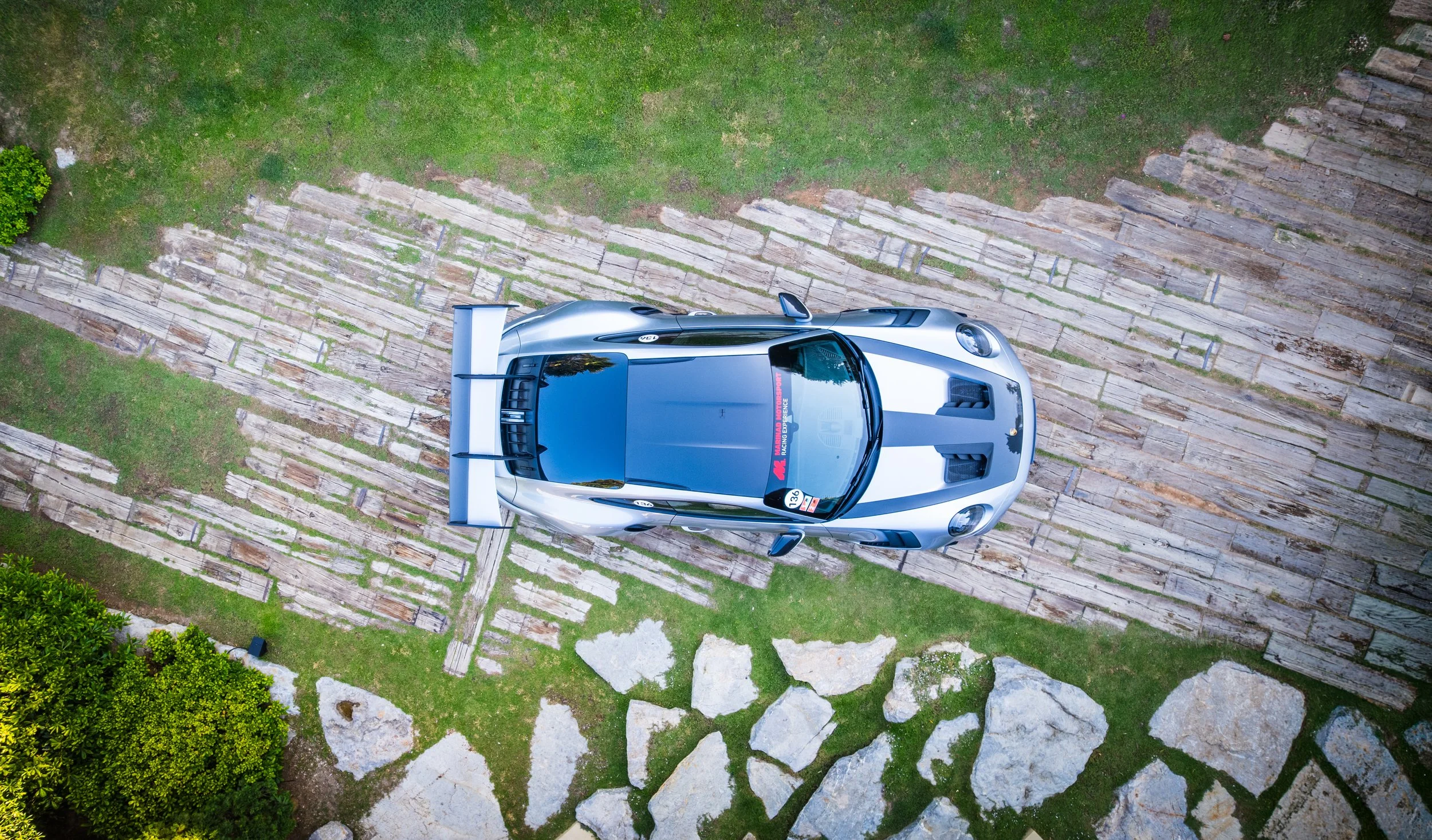 A silver sports car parked on a stone pathway surrounded by green grass and landscaping
