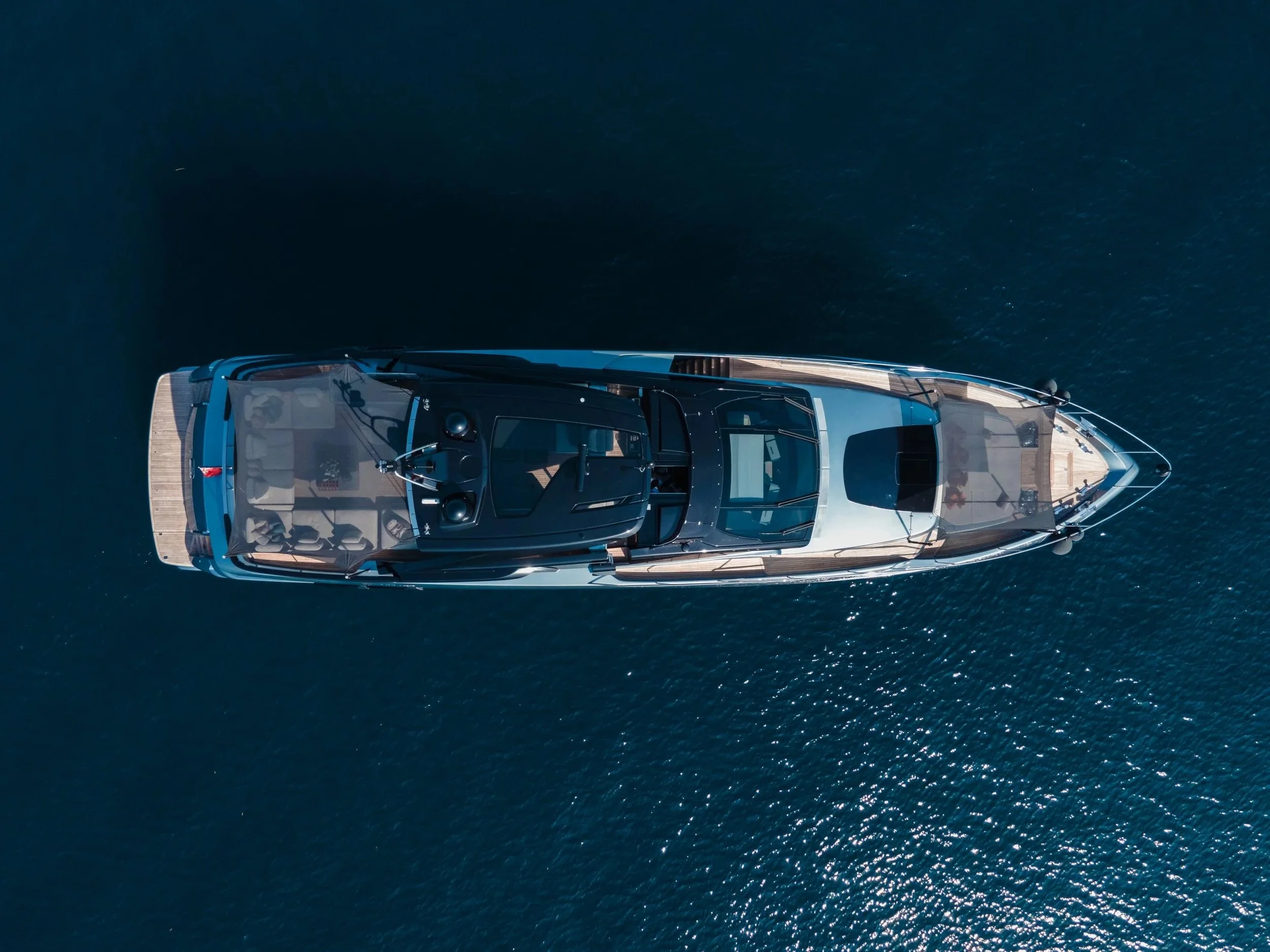 Top-down aerial view of a luxury yacht sailing on deep blue water.