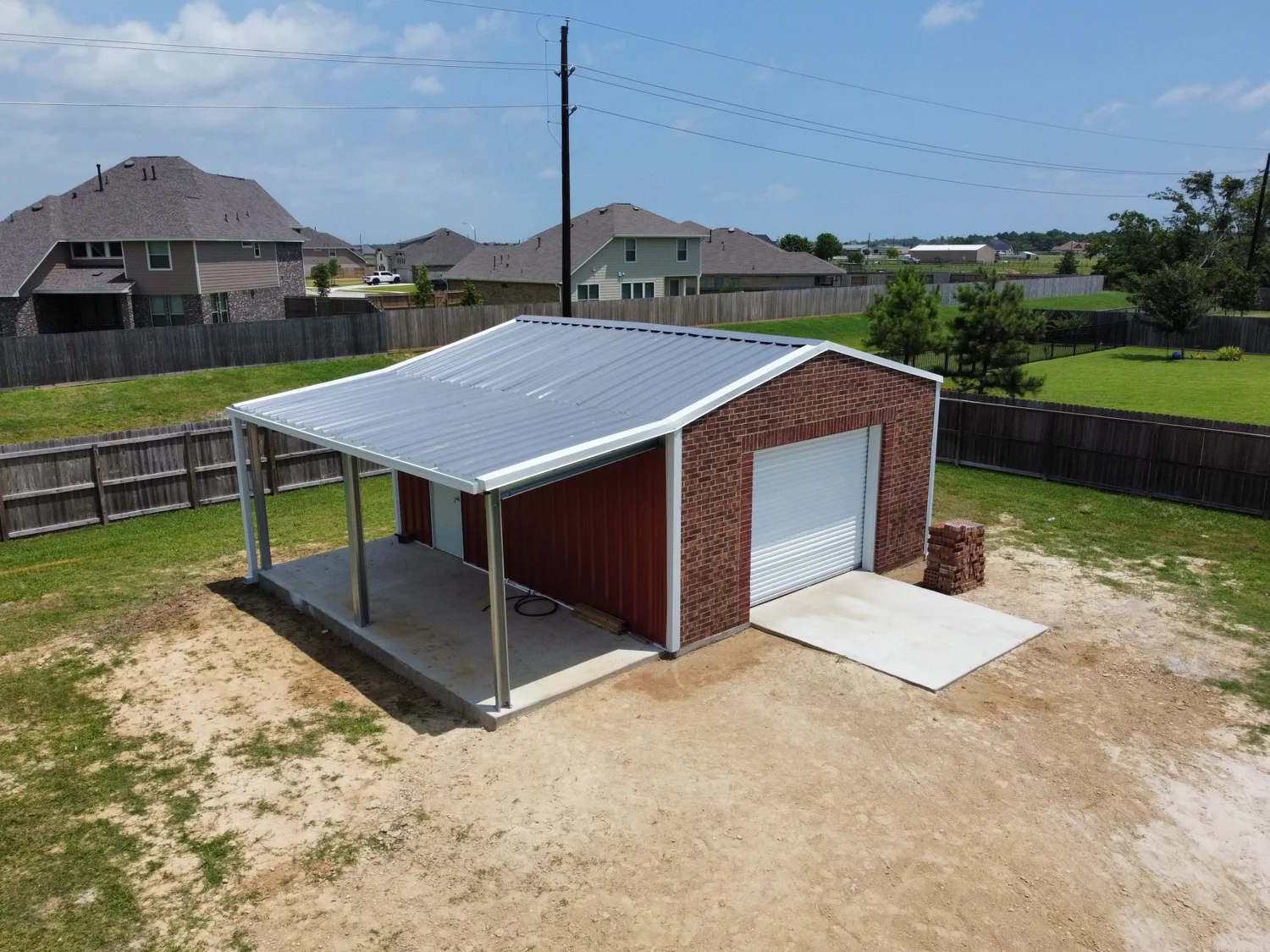 Example of a residential backyard metal garage with a covered work area and brick front.