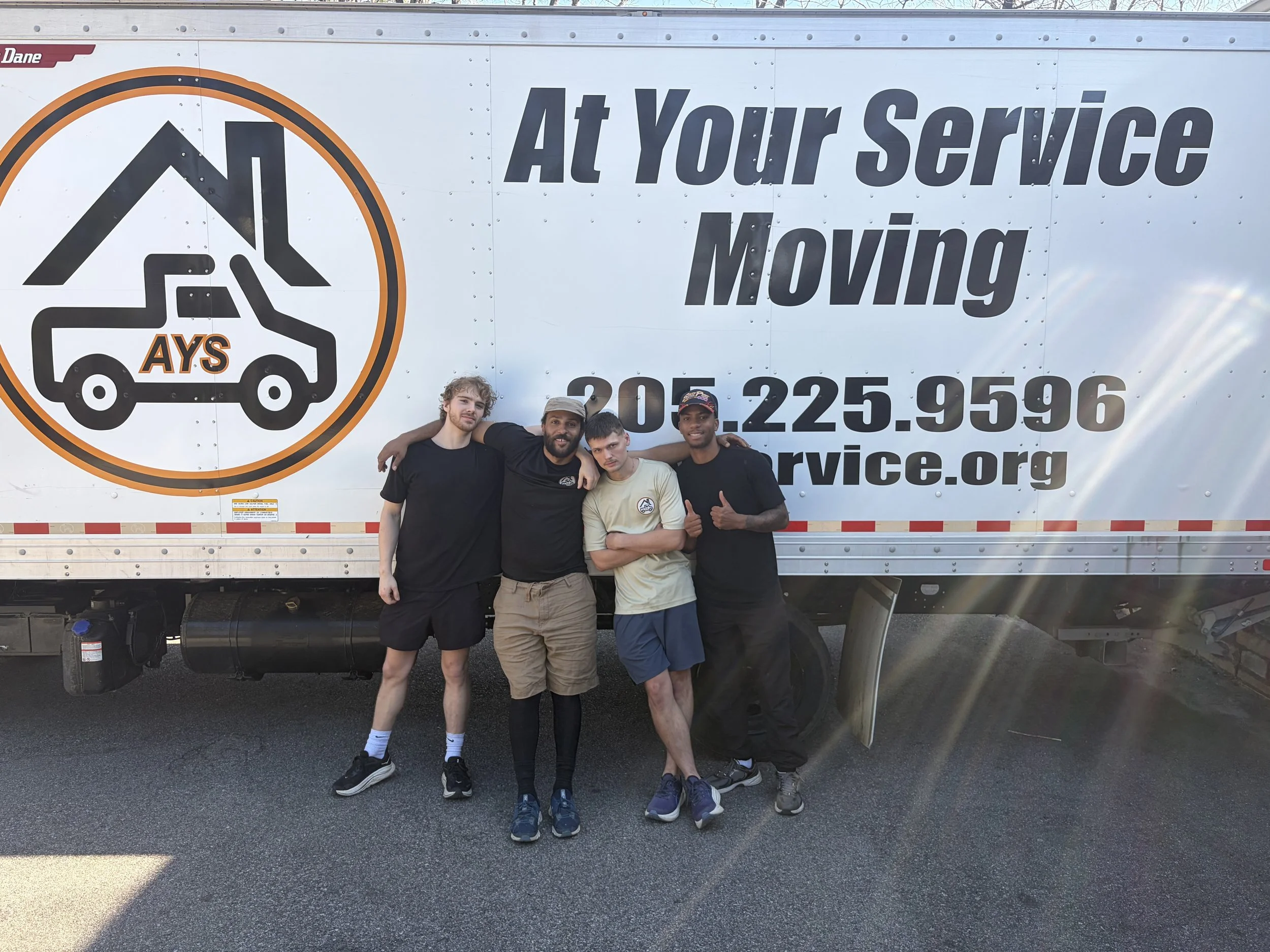 Four men standing in front of a moving service truck, smiling and posing for the camera.