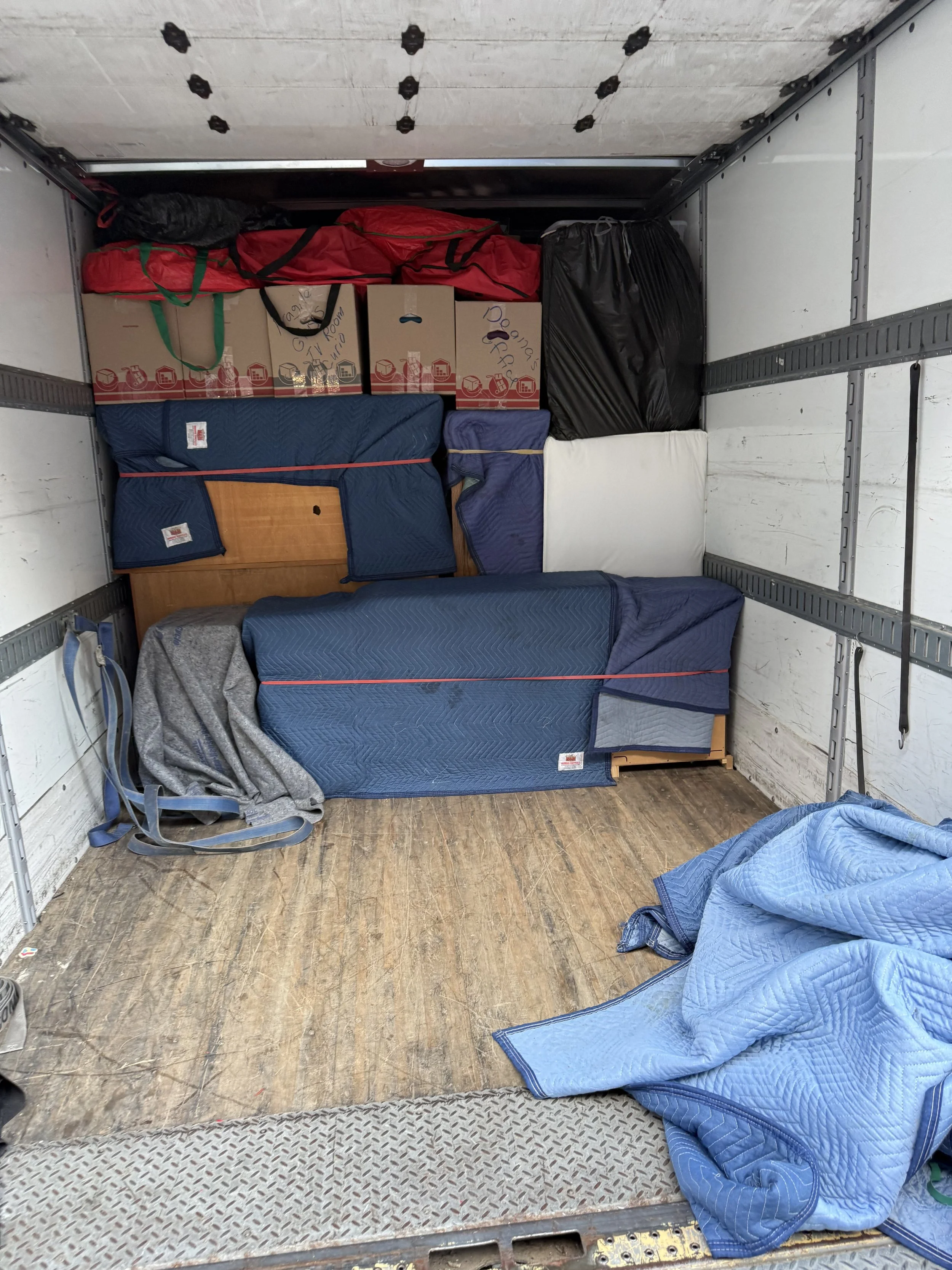 Packed moving truck interior with boxes, furniture, blankets, and bags