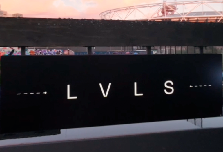Black sign with white letters 'LVLS' and decorative dashed lines on each side, outdoors during sunset.