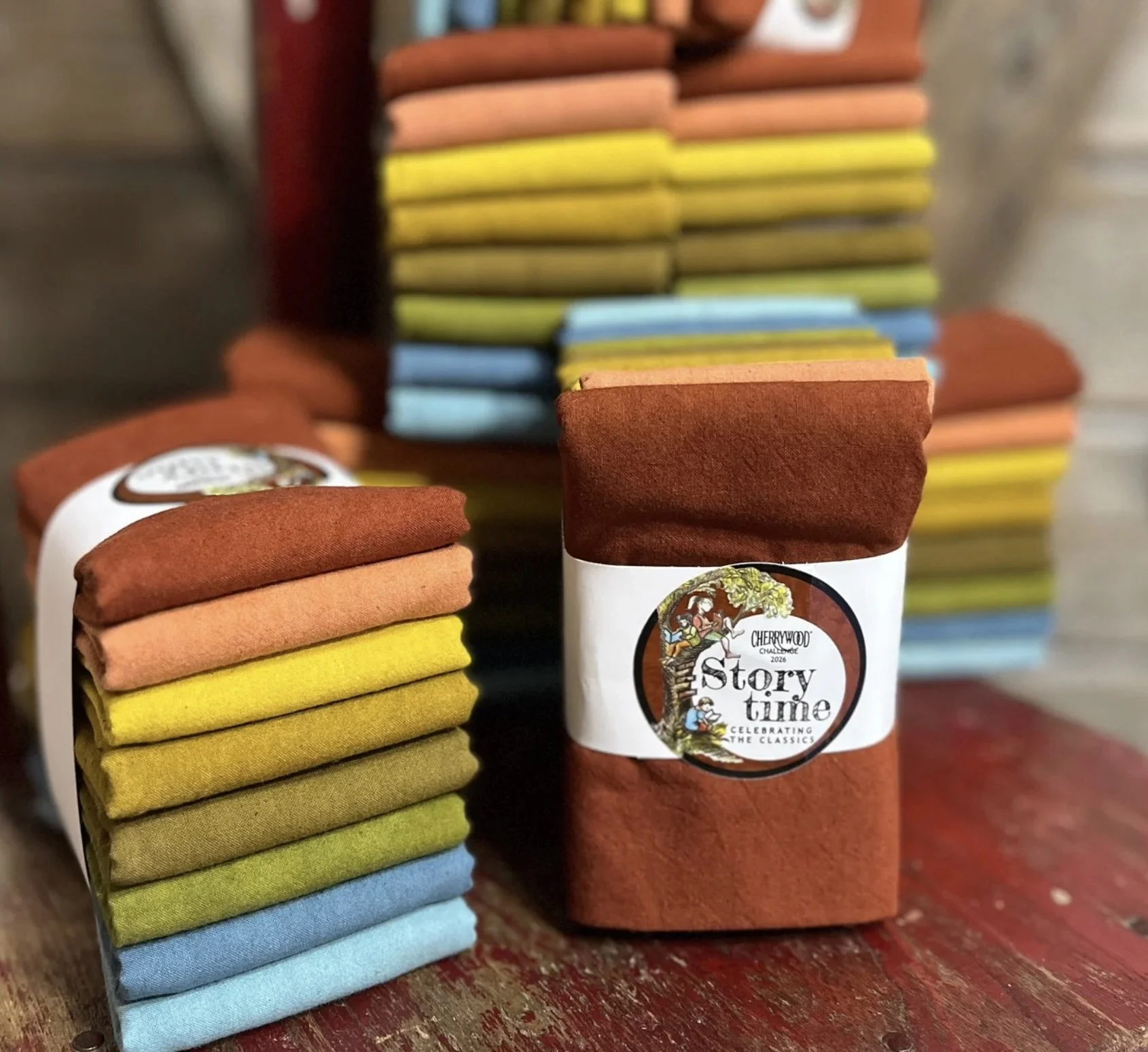 Bundles of the Story Time Challenge Cherrywood fabric sits on a worn wooden table.