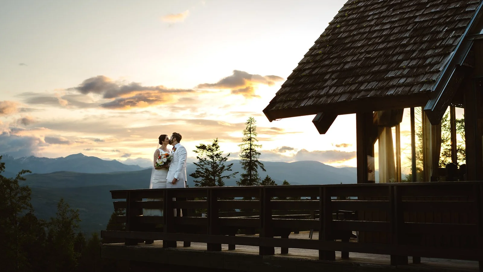 The bride and groom share a romantic kiss outside the venue as the sun sets during their romantic mountain wedding.