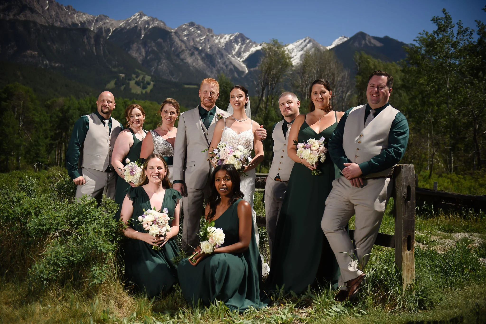 The couple and their wedding party pose closer together for a group portrait at a ski resort wedding with mountains in the background