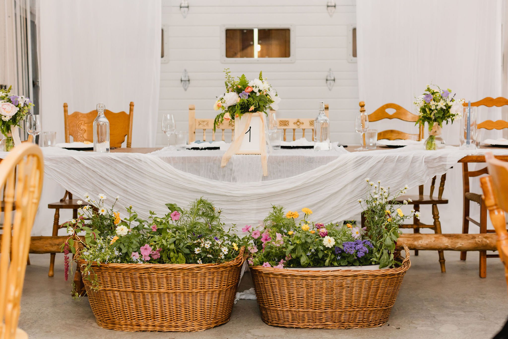 Floral baskets and chiffon-draped head table inside a rustic barn at a Western Chic BC wedding.