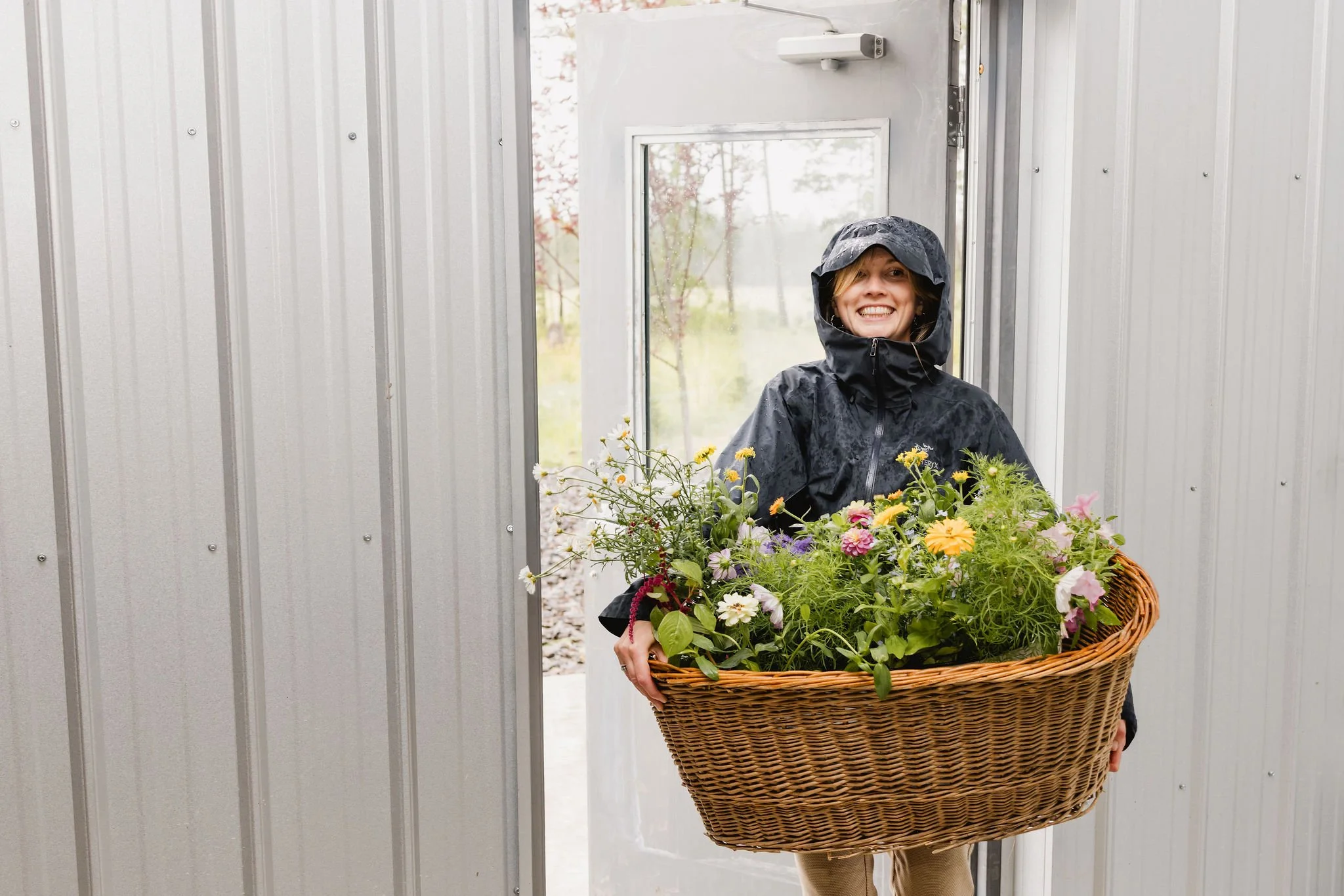 Rosie carrying a basket of wildflowers in the rain during Western chic BC wedding setup.