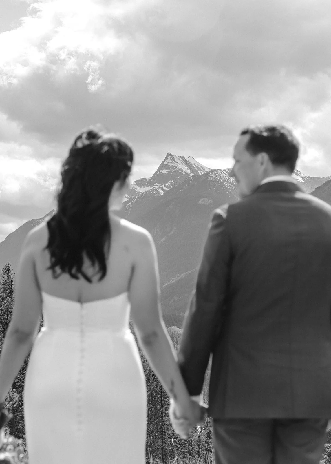 View from behind of a couple during their microwedding restaurant elopement, with the groom facing the bride and mountains in the background