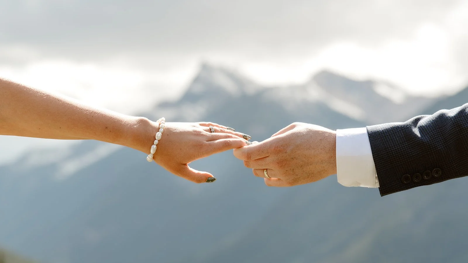 Close-up of a couple touching hands during their microwedding restaurant elopement with mountains in the background