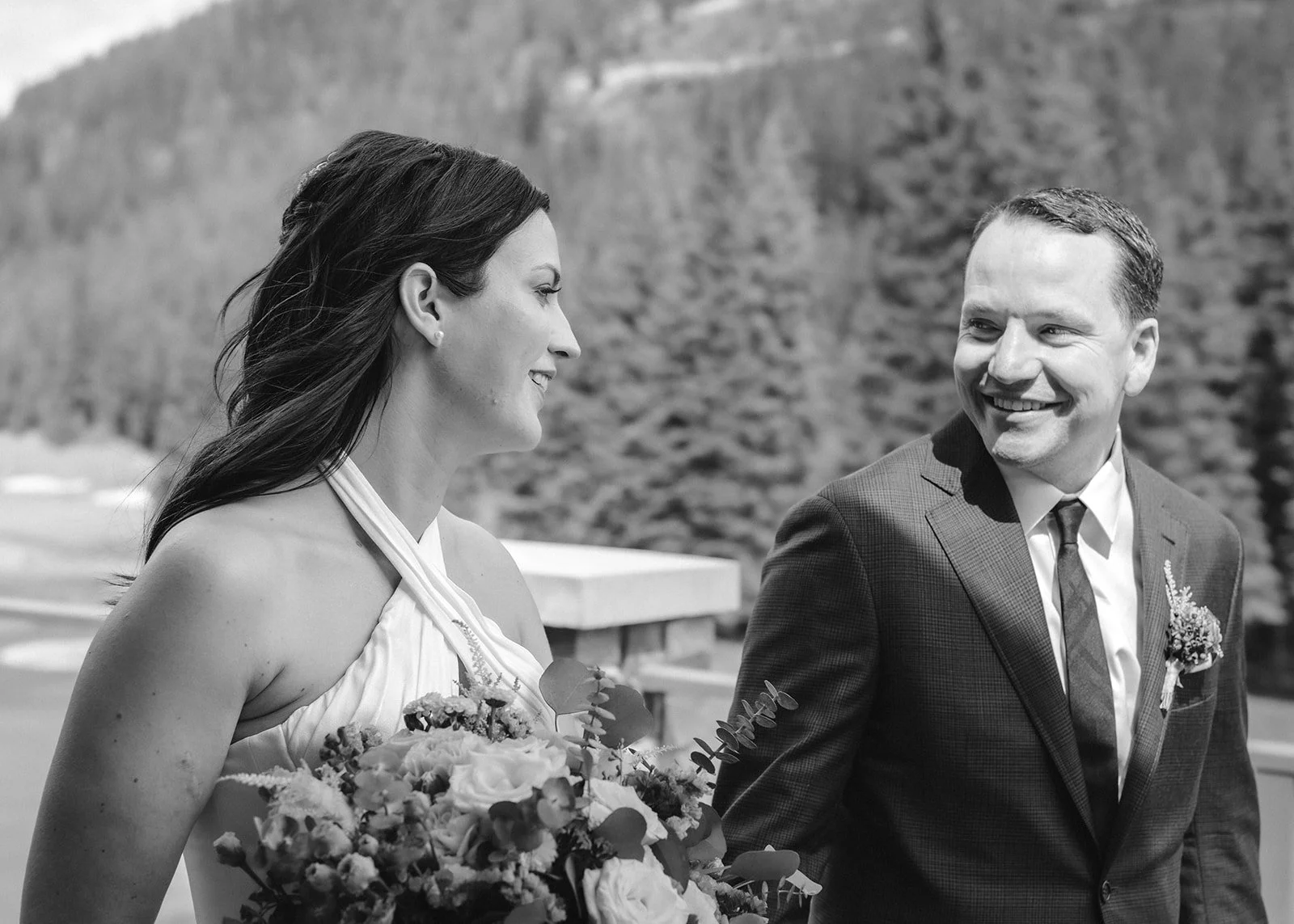 Portrait of a couple smiling at each other during their micro wedding restaurant elopement, set against tree-filled scenery.