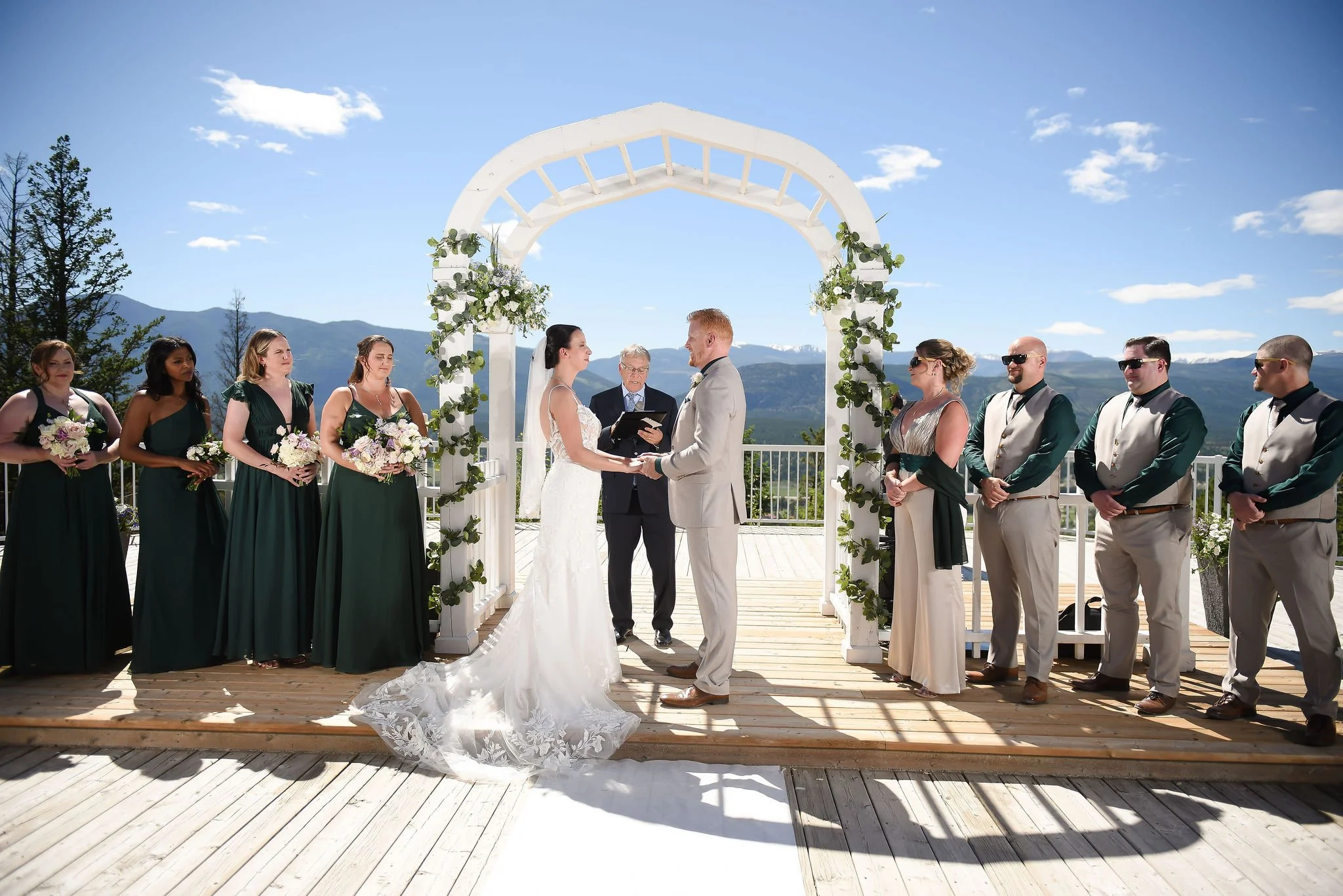 The bride and groom hold hands at the altar with their wedding party standing beside them during a ski resort wedding