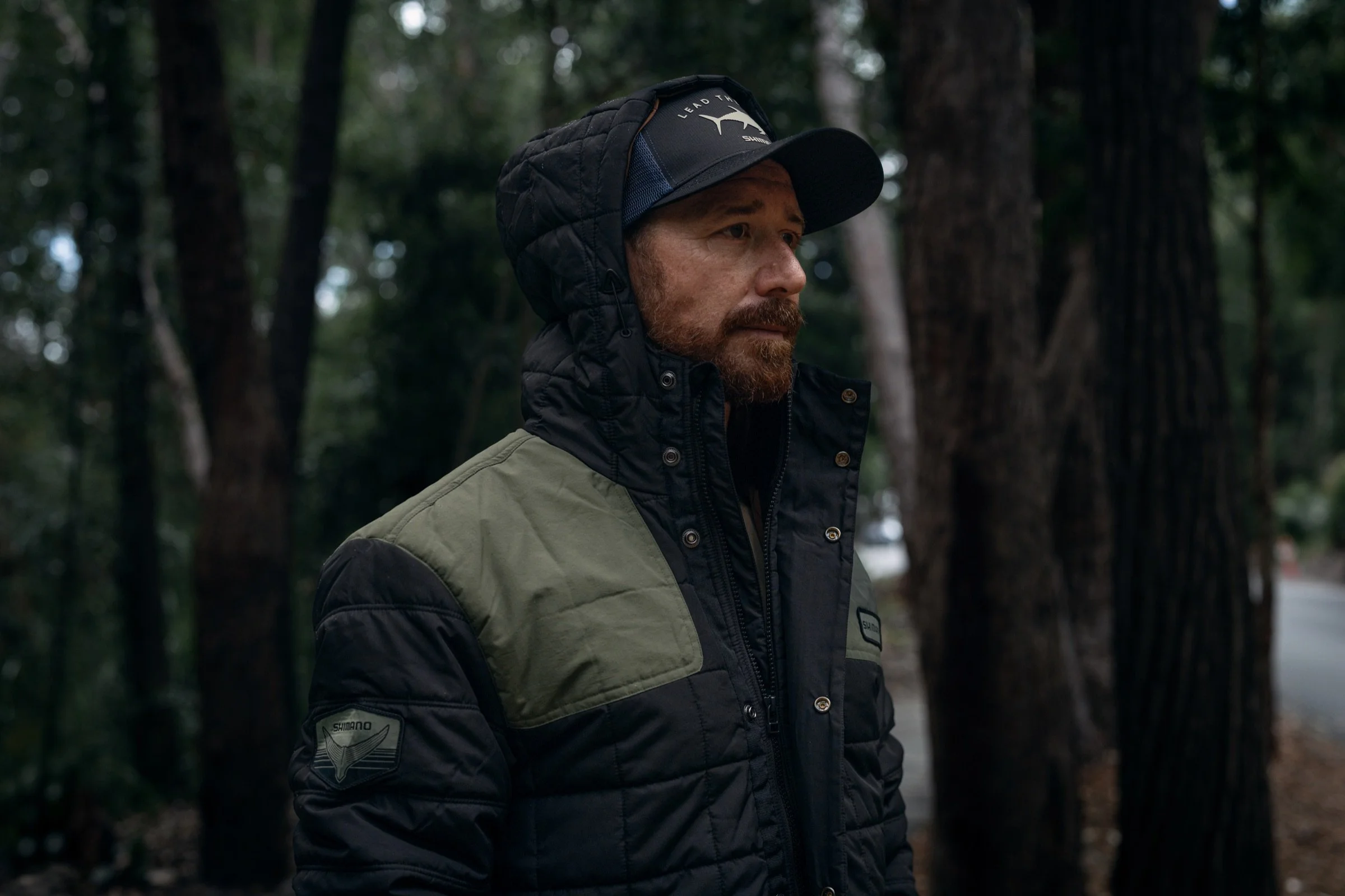 A man wearing a Shimano winter jacket and cap in a forest.