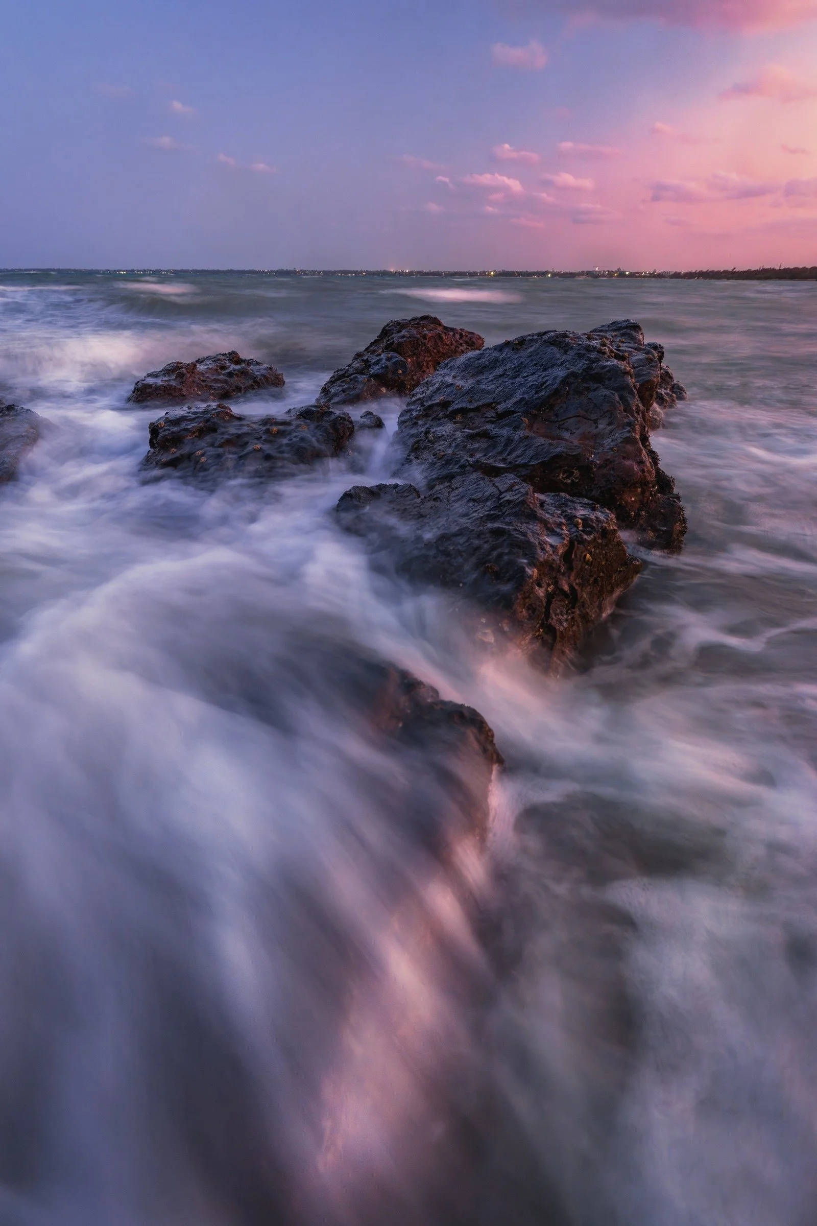 Soft trails of water flow around the rocks at Point Vernon beneath a pastel evening sky in this portrait coastal composition.