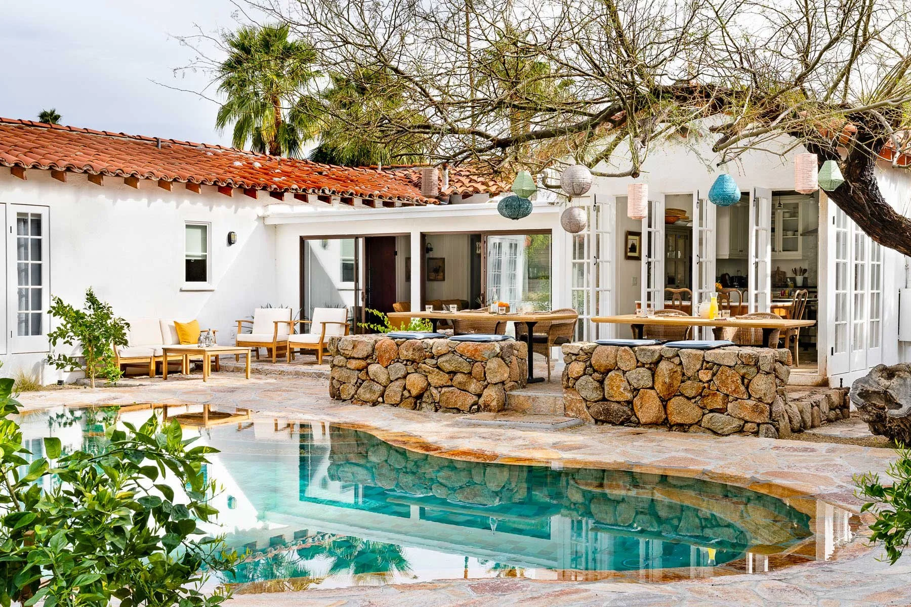 Auric House in Palm Springs. A luxurious, historic 6-bedroom villa managed by Korakia Pensione and Fieldtrip, located near the San Jacinto Mountains. A backyard patio with a swimming pool and open French doors. Wild Thing Yoga, Lauren Clark