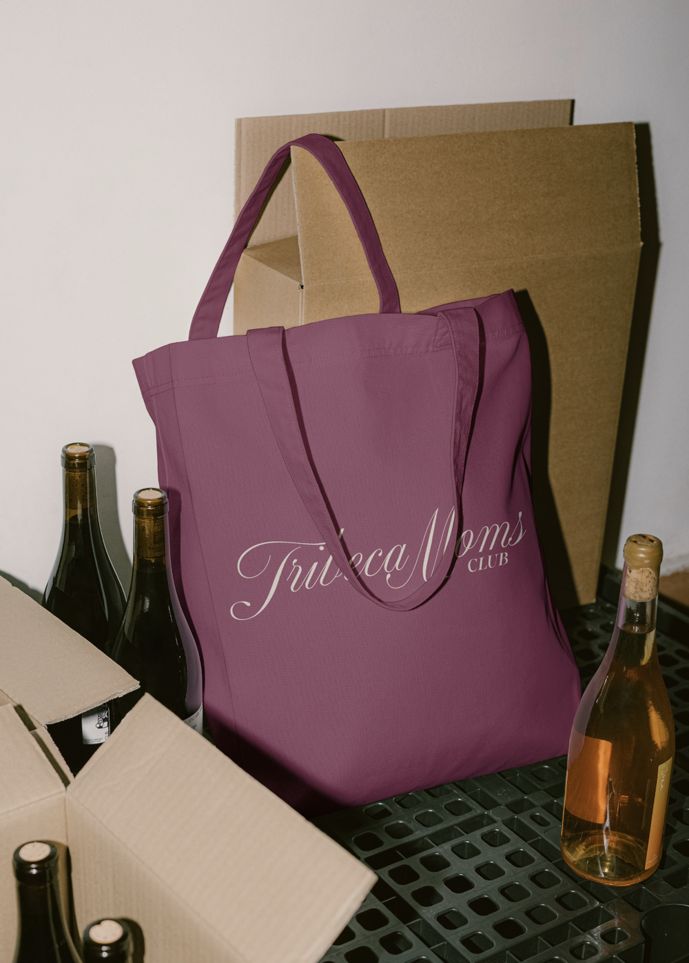 A magenta tote with the script logo, between wine bottles