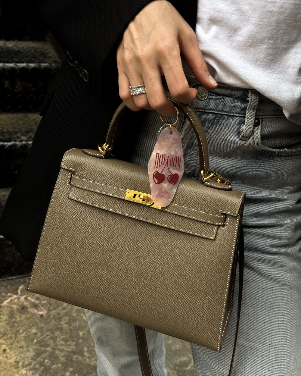 The pink HOT MOM keychain on a taupe bag