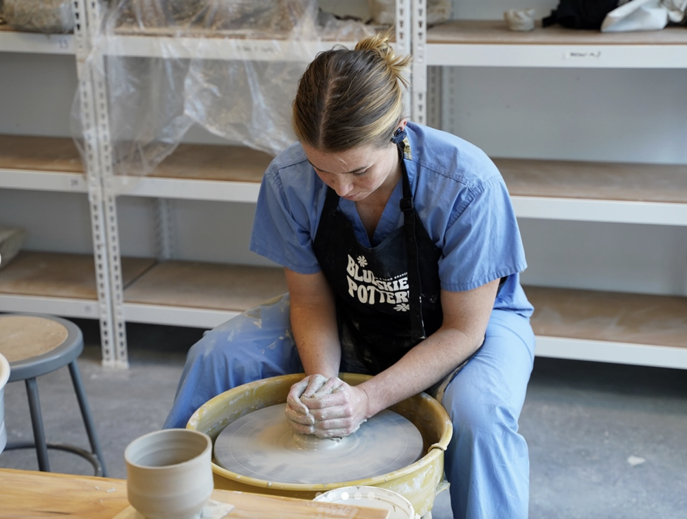 A student at the wheel in a Blue Skies Pottery apron