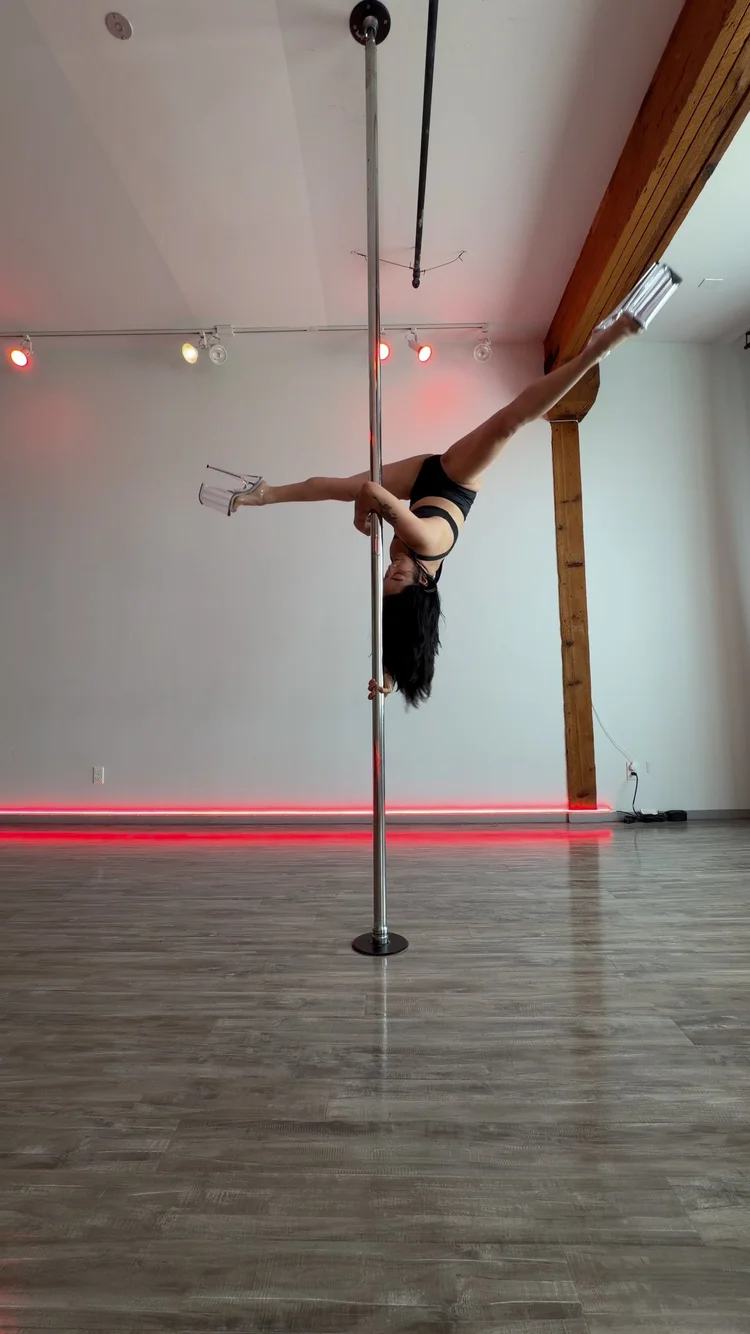 Camille mid-trick on the pole in a bright studio