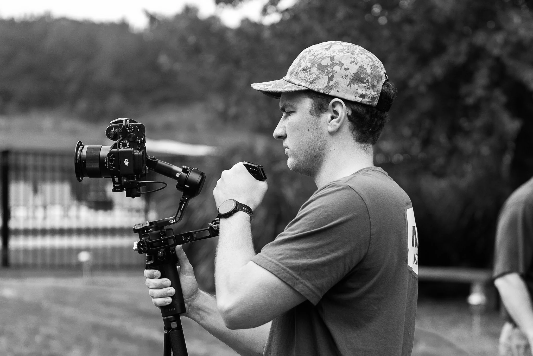Bradley Gossett operating a professional camera mounted on a stabilized rig outdoors, with trees in the background.