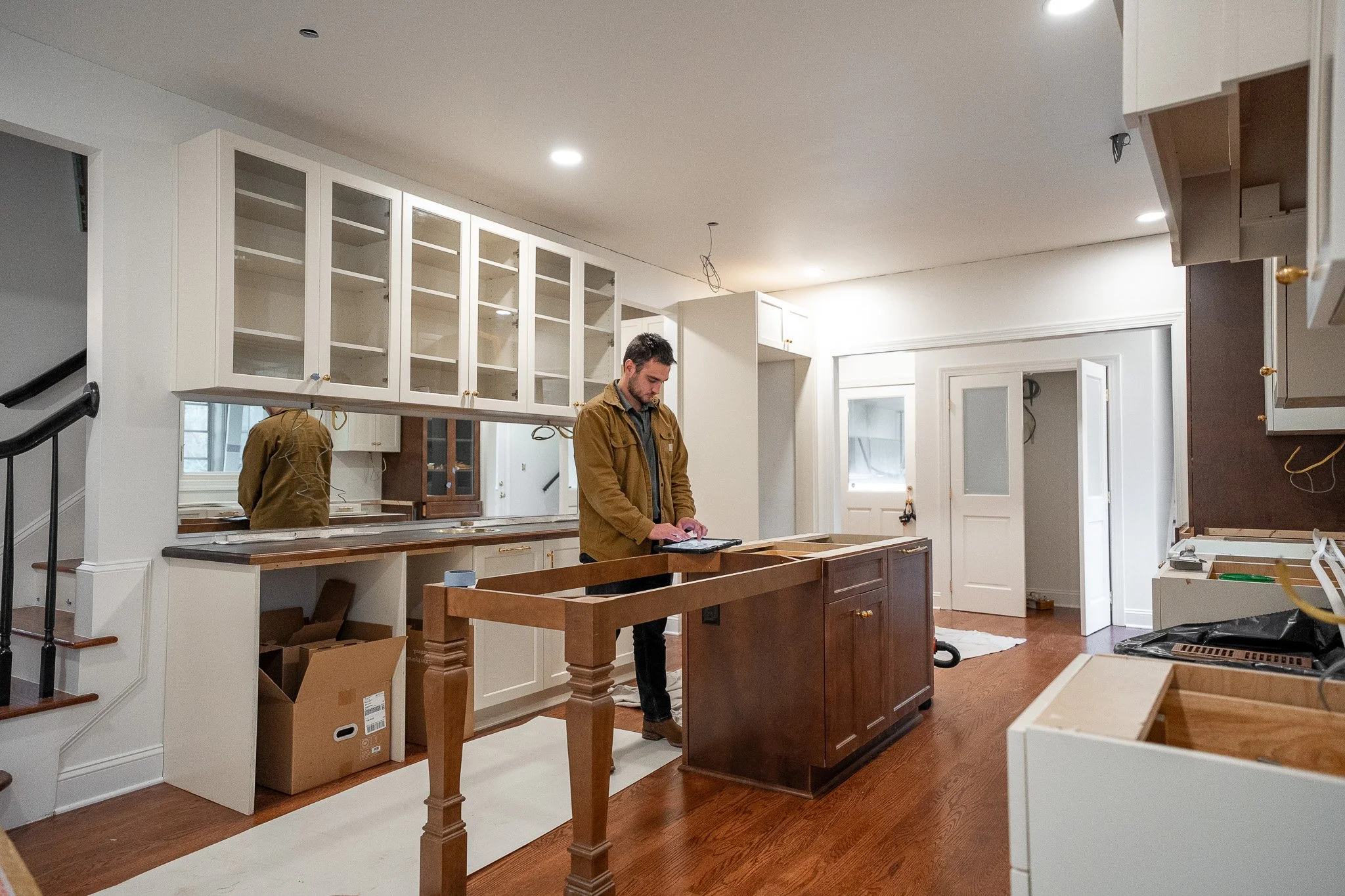 A man standing in a kitchen under renovation, looking at a tablet, surrounded by unfinished cabinets and construction materials.
