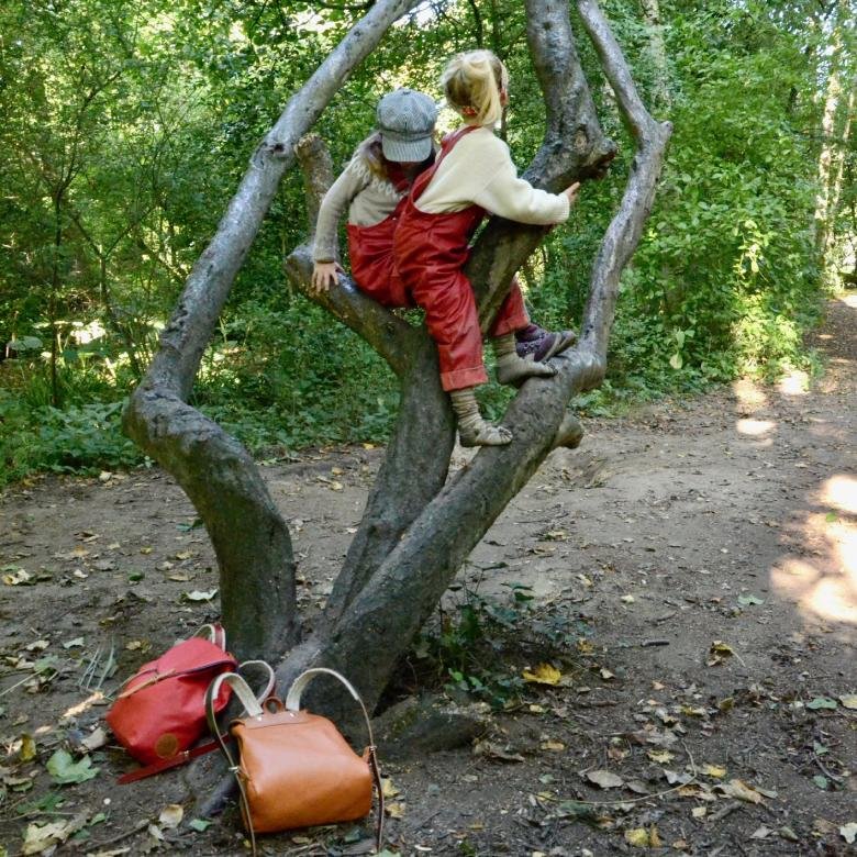 Two girls are climbing a tree, and they're wearing lederhosen.