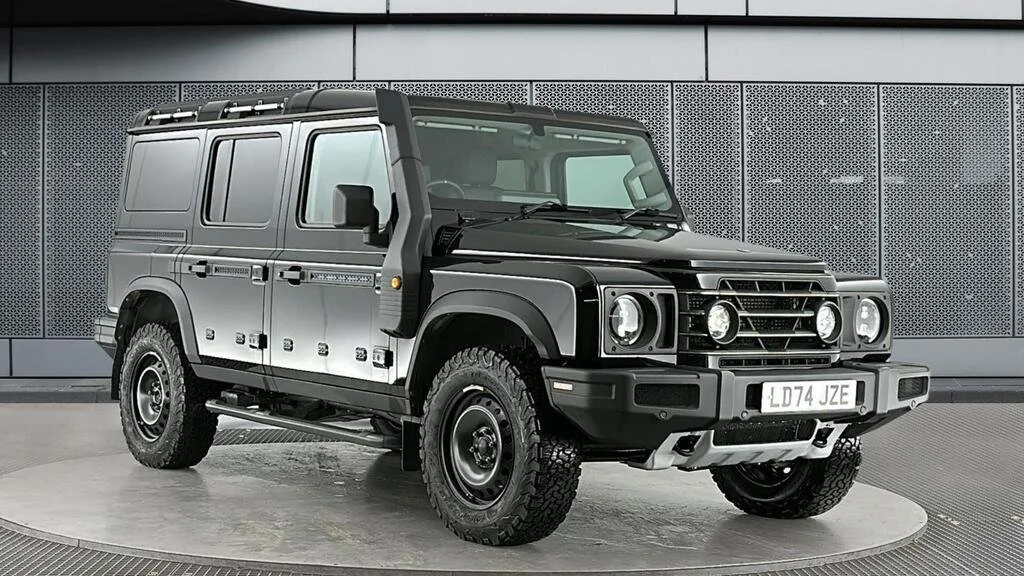 Black Land Rover Defender SUV parked indoors against a metallic wall.