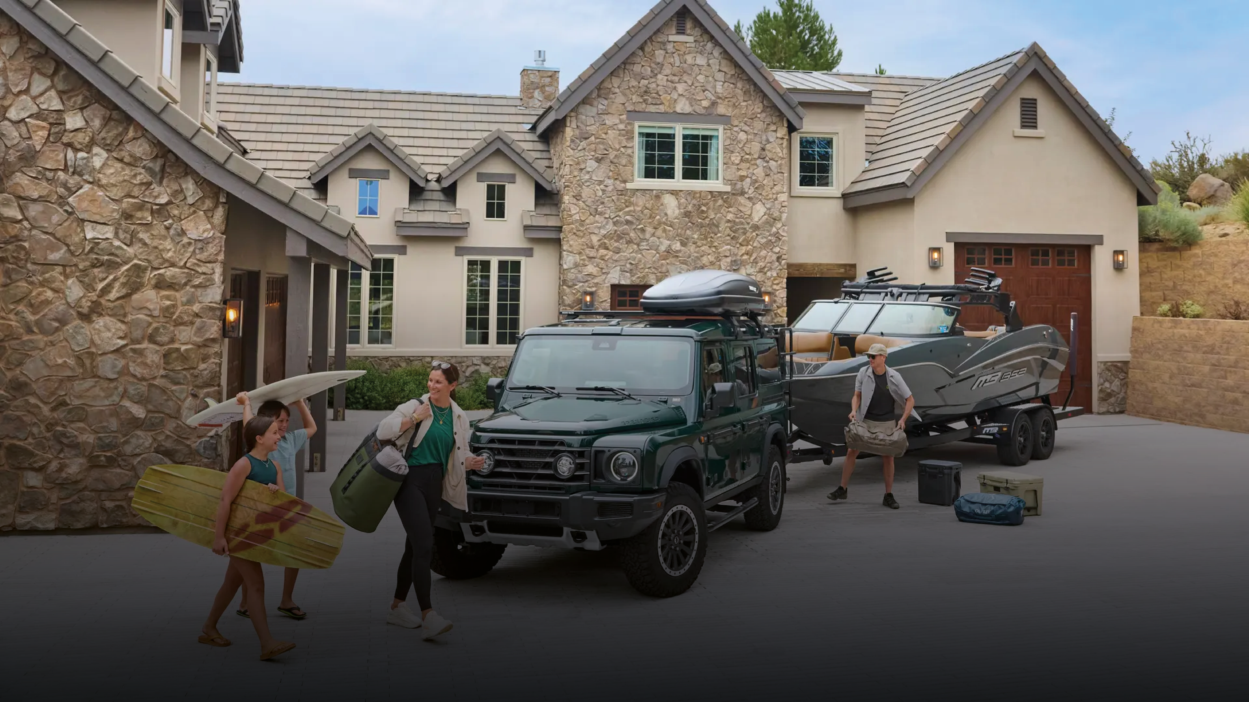 aFamily loading surfboards and kit into a green INEOS Grenadier Station Wagon outside their home