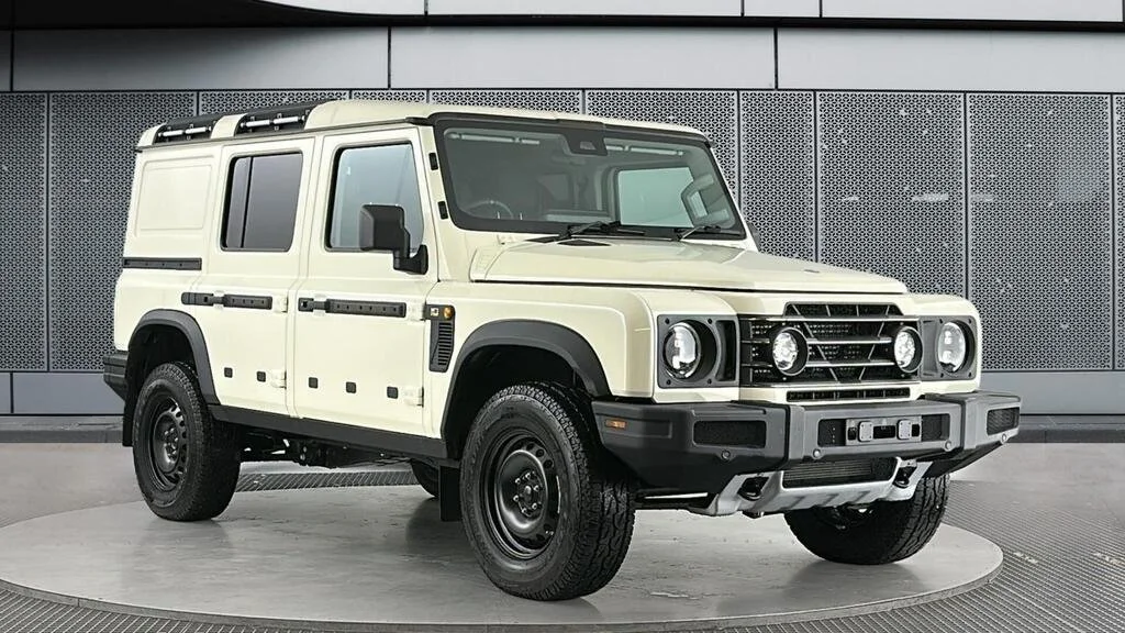 A beige four-door off-road SUV with black wheels displayed indoors on a circular platform.