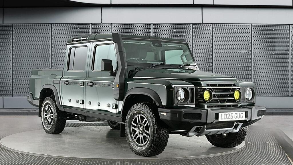 A black off-road pickup truck with yellow fog lights on the front grille, parked on a circular platform indoors with a metallic wall background.