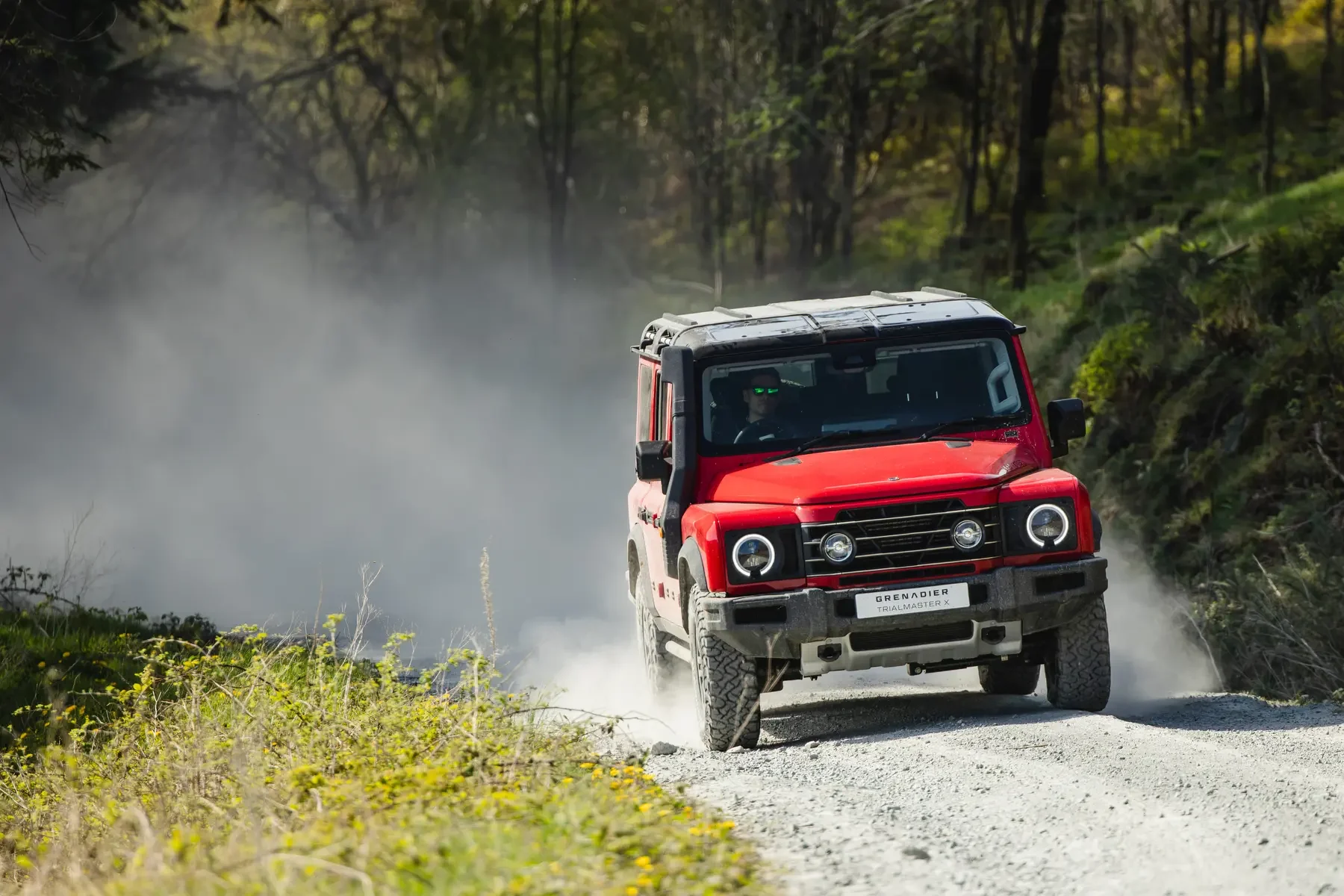 Red INEOS Grenadier driving off-road on a dusty gravel track