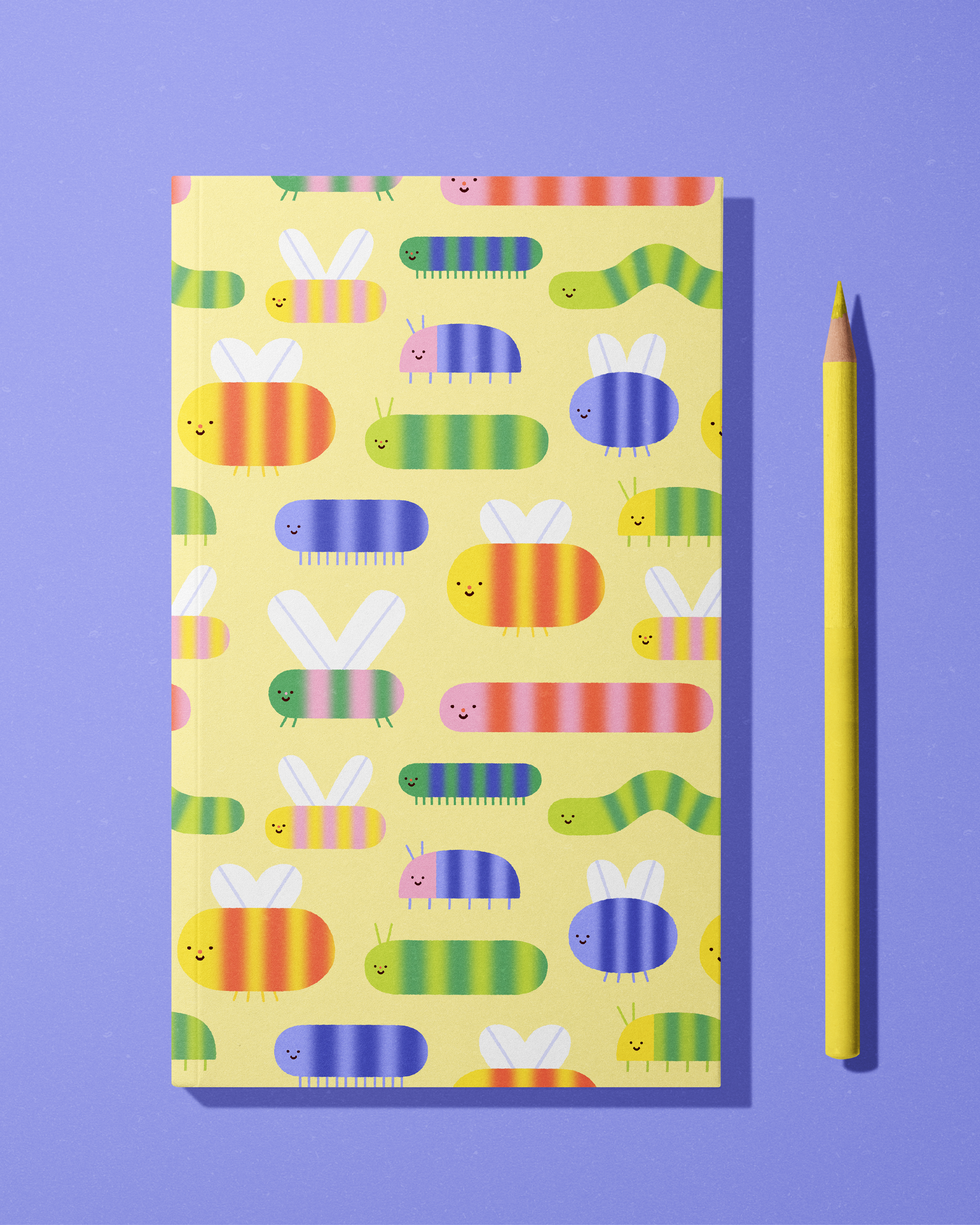 A colorful notebook featuring a pattern of happy, cartoon-like caterpillars and bunny shapes on a yellow background, placed on a purple surface with a yellow pencil beside it.