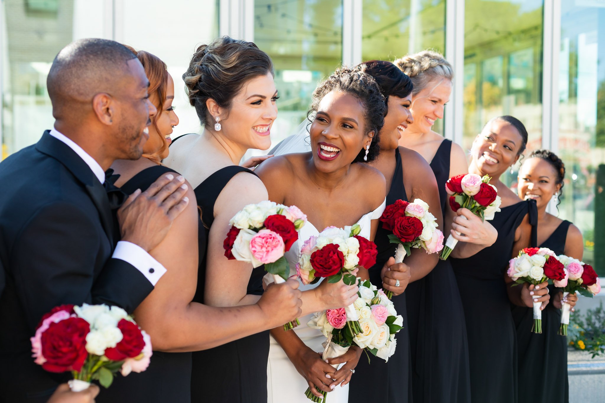 A bride smiling with her attendants holding pink red and white bouquets in Texas The Amber Studio