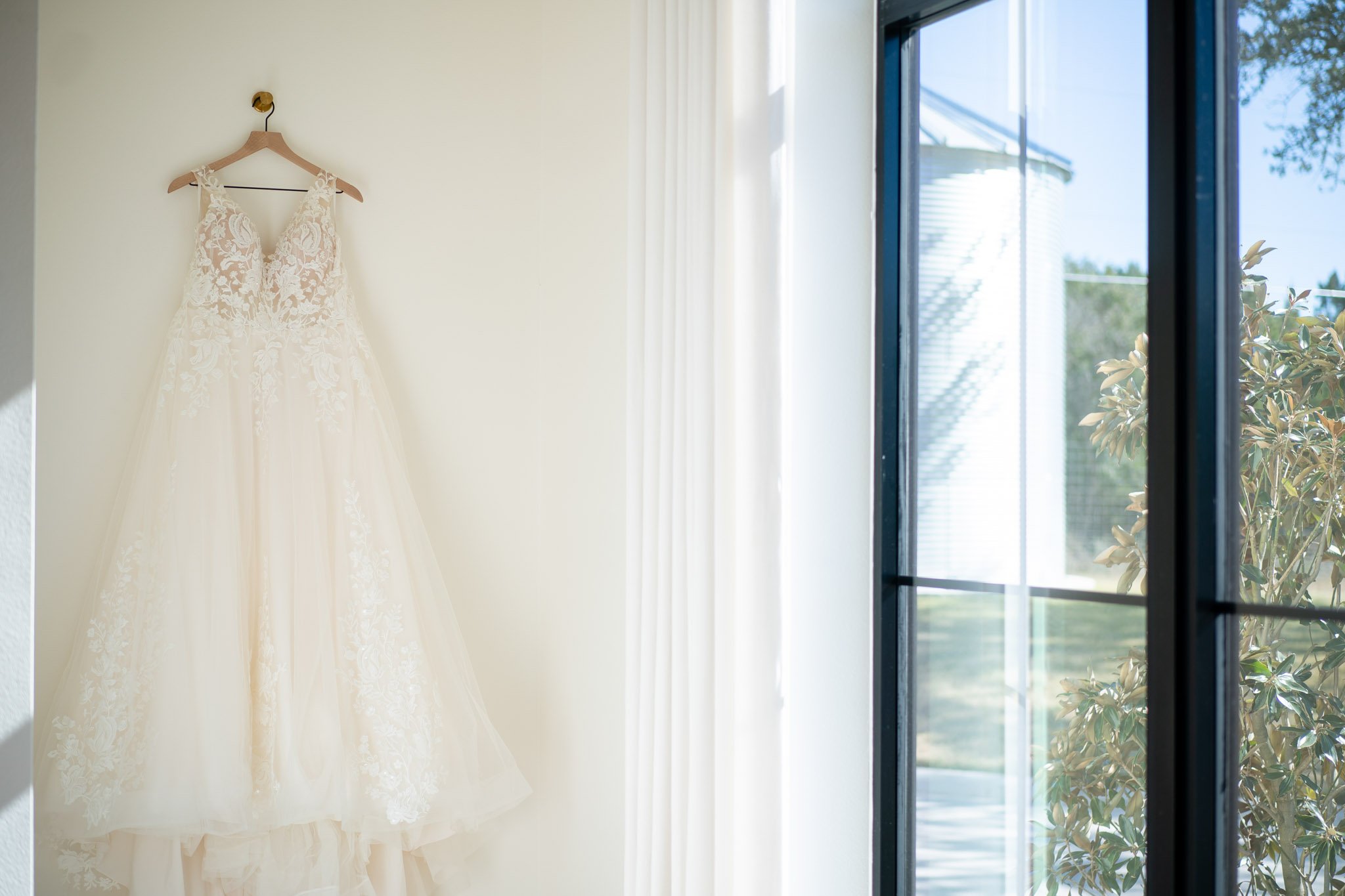 An A line lace wedding dress hanging on a hanger by a window at the Arlo Austin TX The Amber Studio
