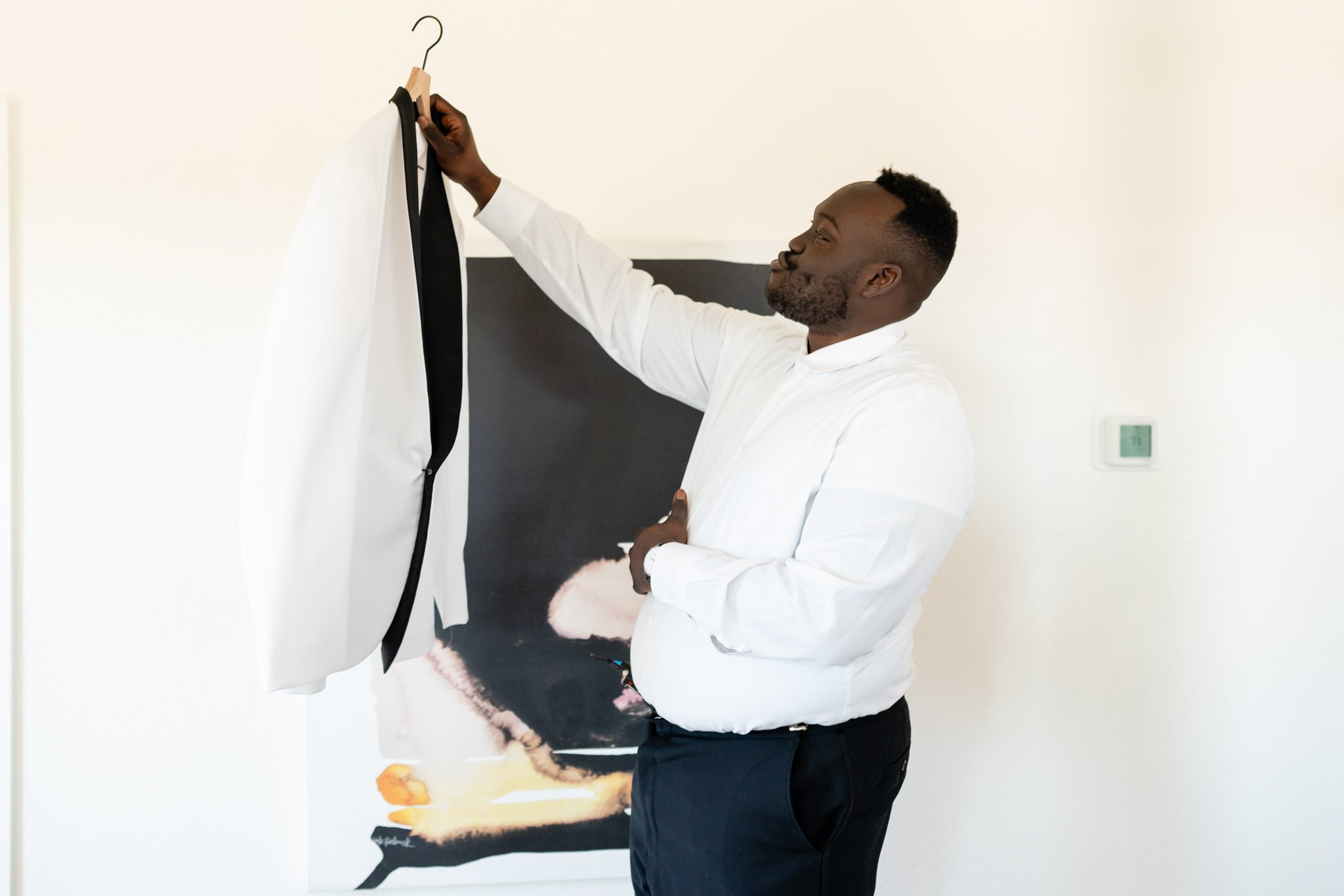 Black groom holding up the suit jacket on a hanger at The Arlo in Austin Texas The Amber Studio