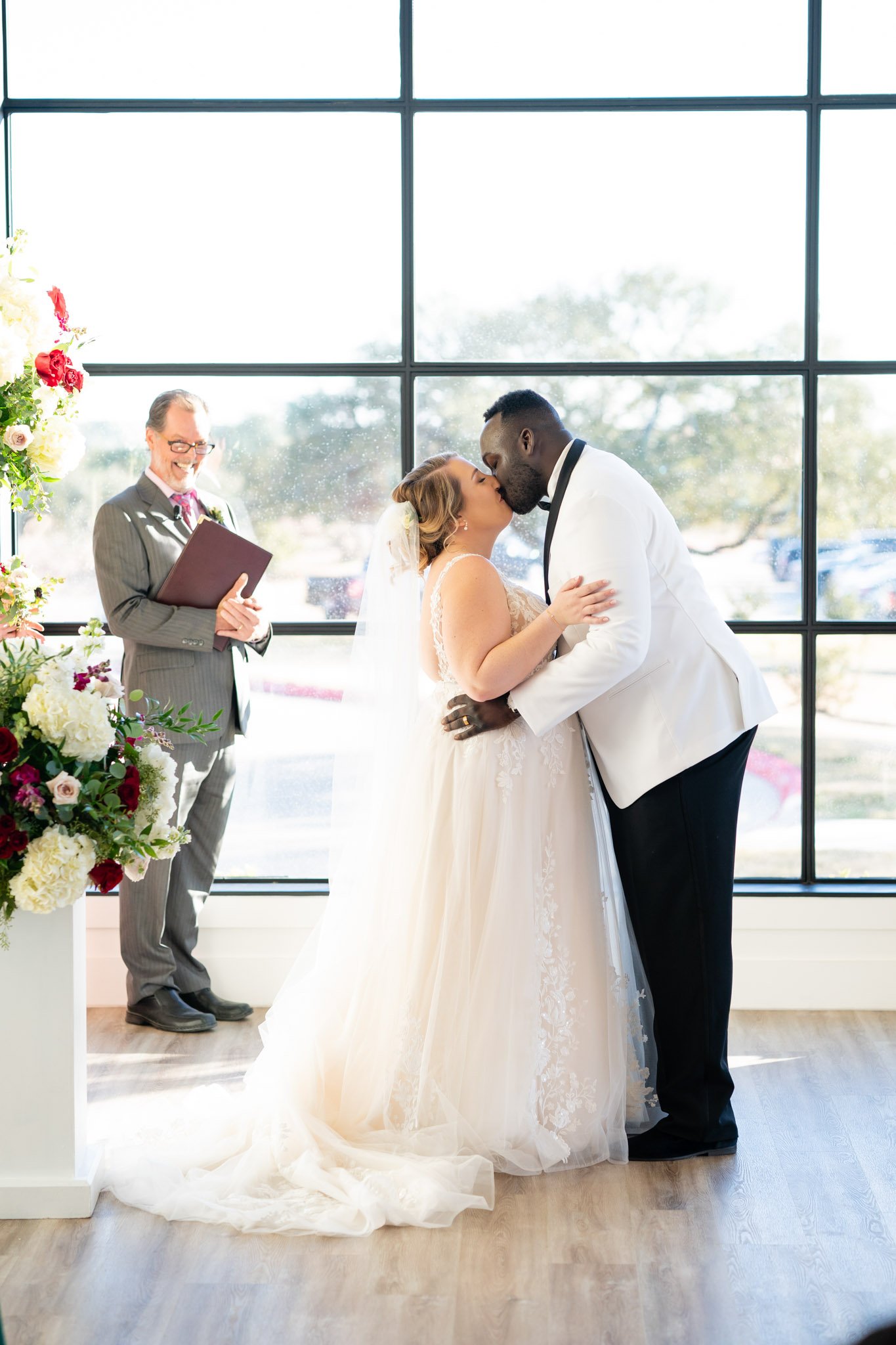Multiracial newlyweds kiss at the wedding ceremony before a big window at the Arlo TX The Amber Studioa