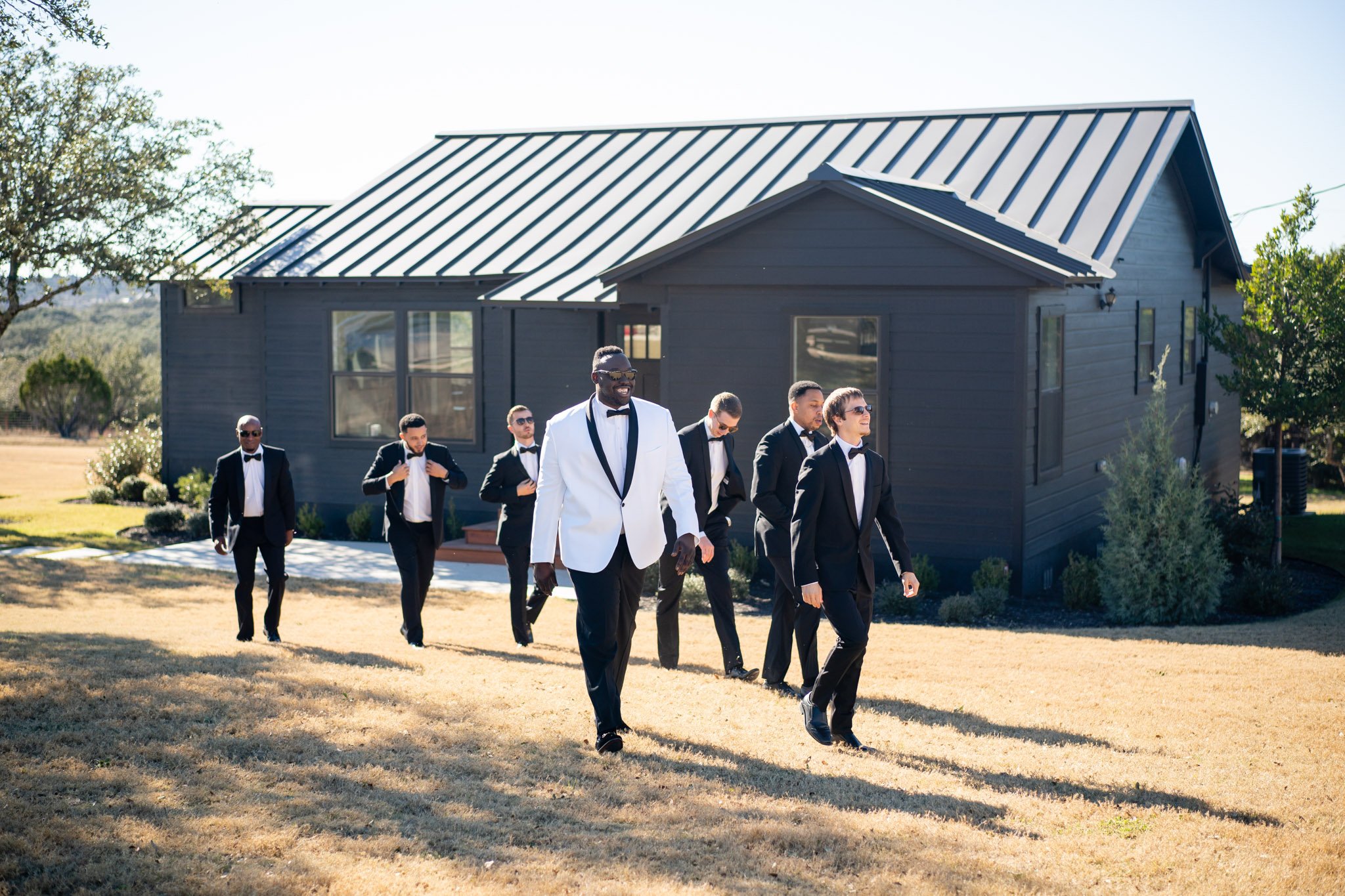 The groom in a white suit jacket walks with groomsmen in black suit jackets at the Arlo The Amber studio