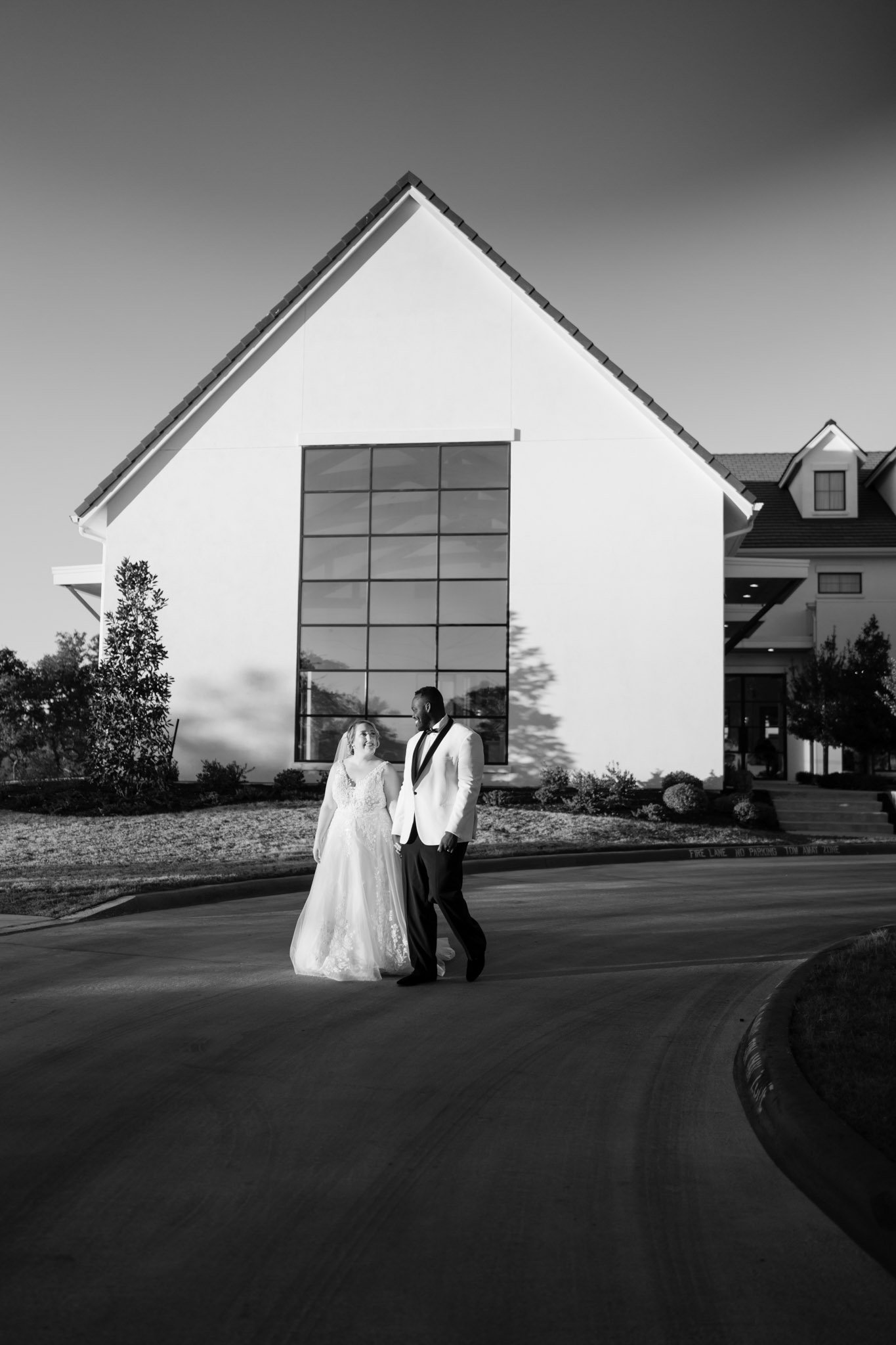 Newlyweds walk hand in hand before a large white building The Arlo Austin TX The Amber Studio