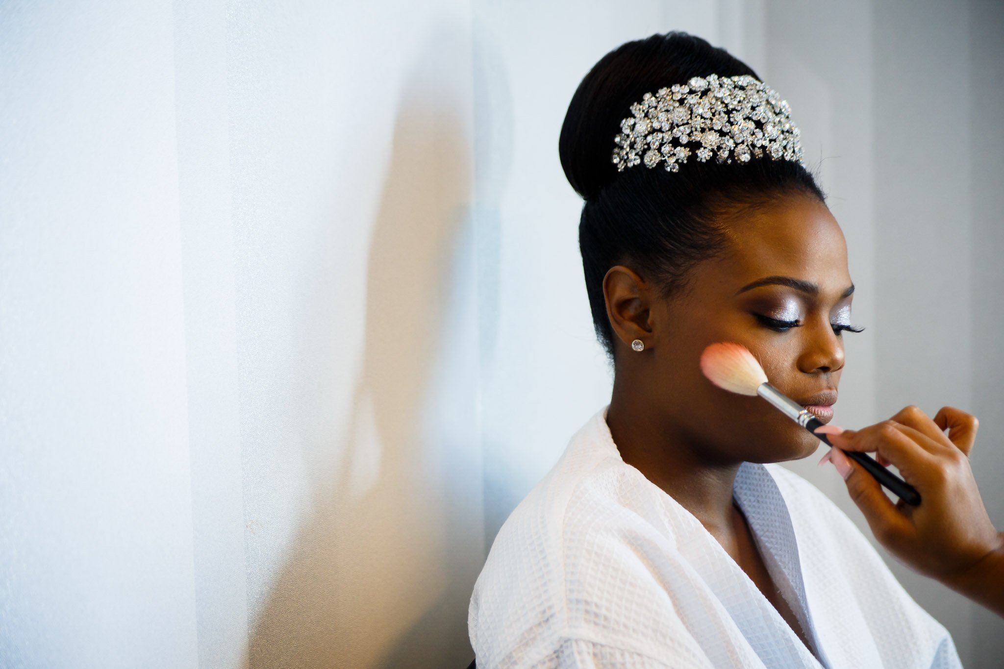 A black bride with an updo getting their makeup done while wearing a robe in DFW Texas the Amber Studio