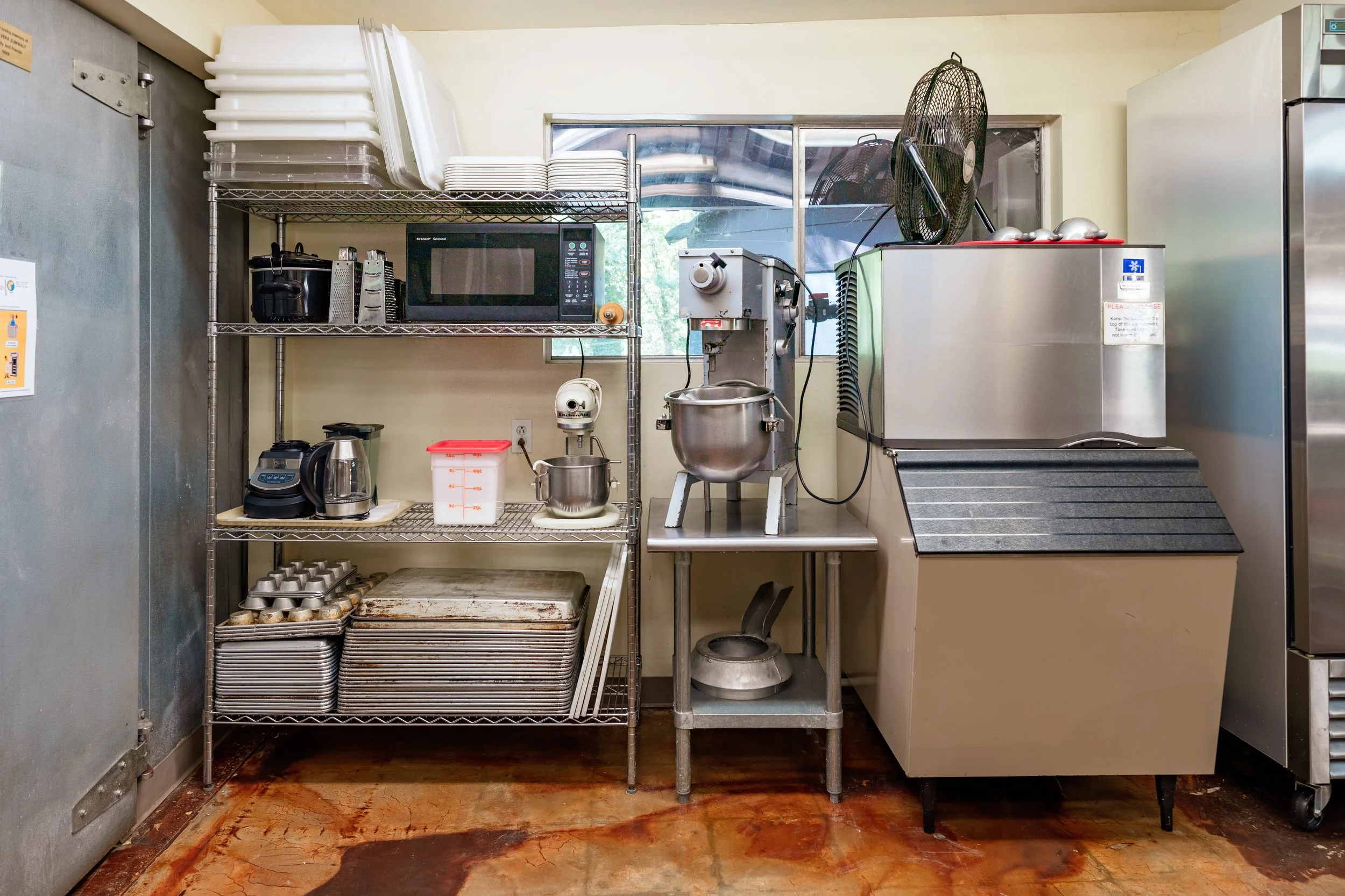 Section of the kitchen with a microwave, crockpot, baking sheets, mixers, and an ice machine.