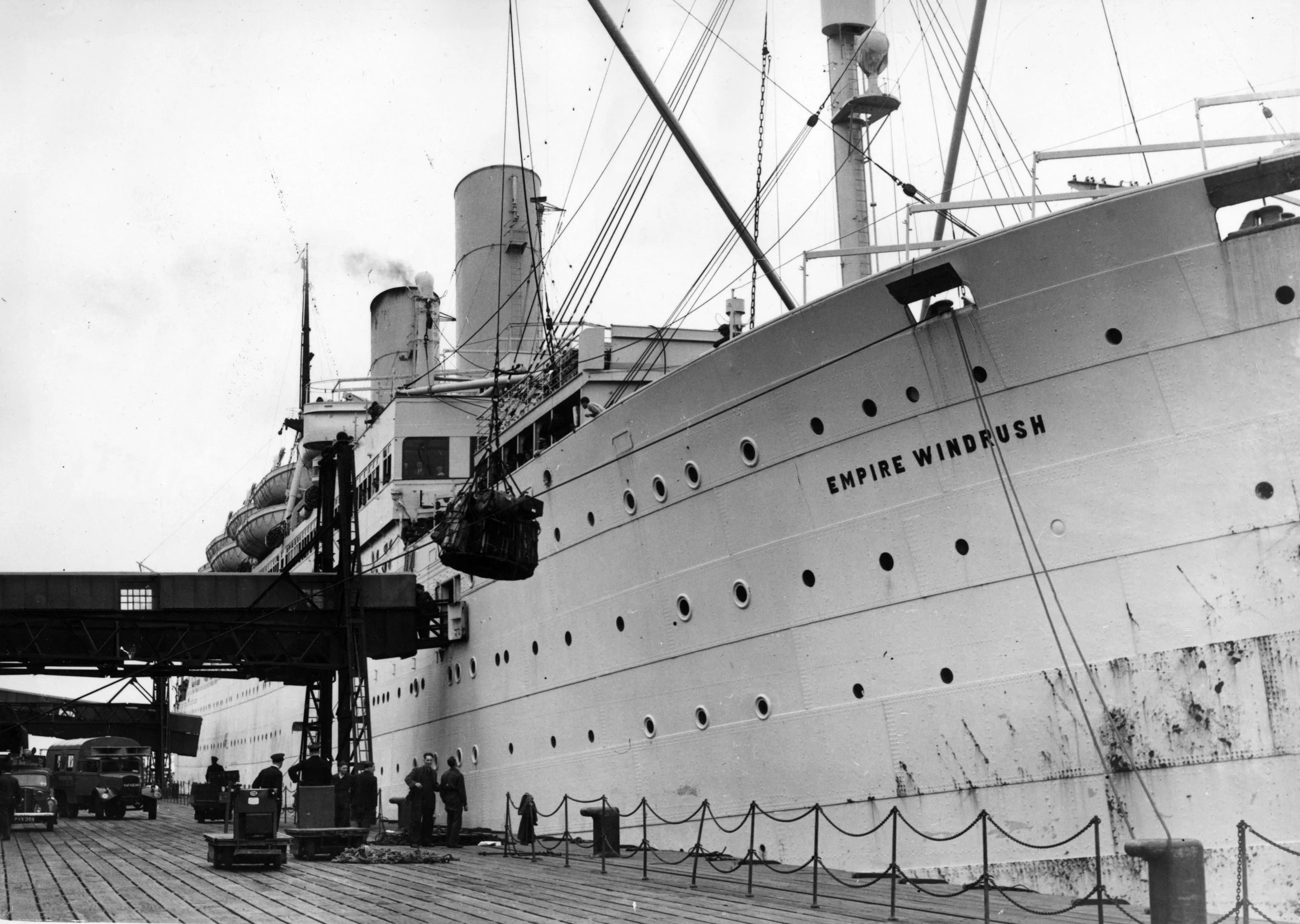 Black and white photo of the cruise ship Empire Windrush docked at a pier, with workers and vehicles nearby.
