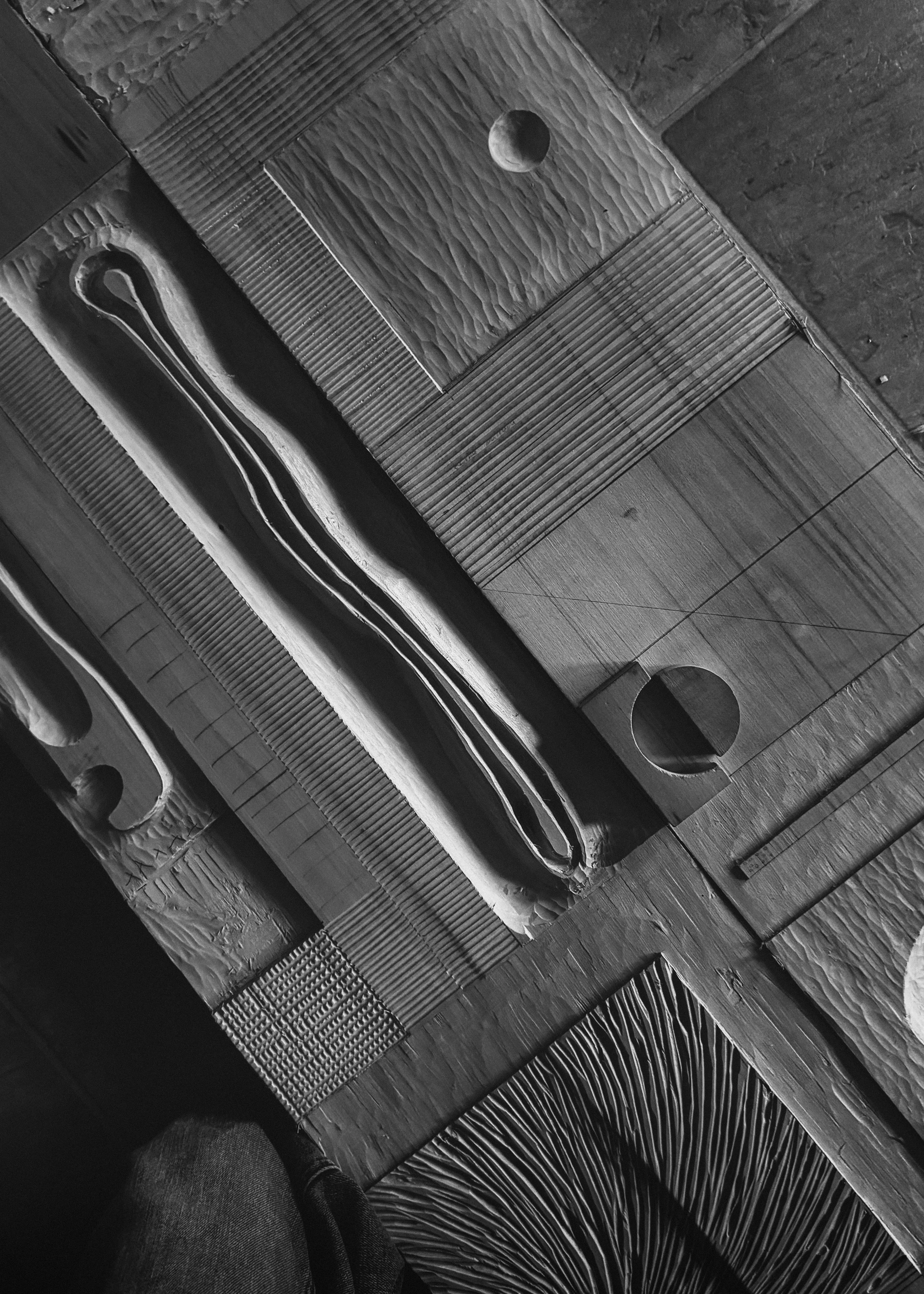 Overhead detail of a wood relief sculpture showing the interplay of light and shadow on smooth circular indents and sharp linear textures.