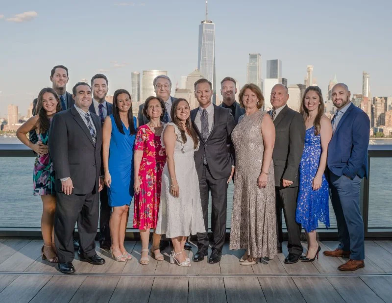 Rooftop wedding group photo with couple and guests, city skyline view and waterfront backdrop