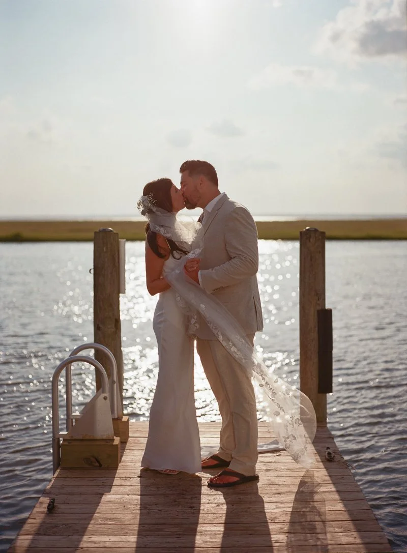 Bride and groom sharing a kiss on a dock with sunlight reflecting across the water.